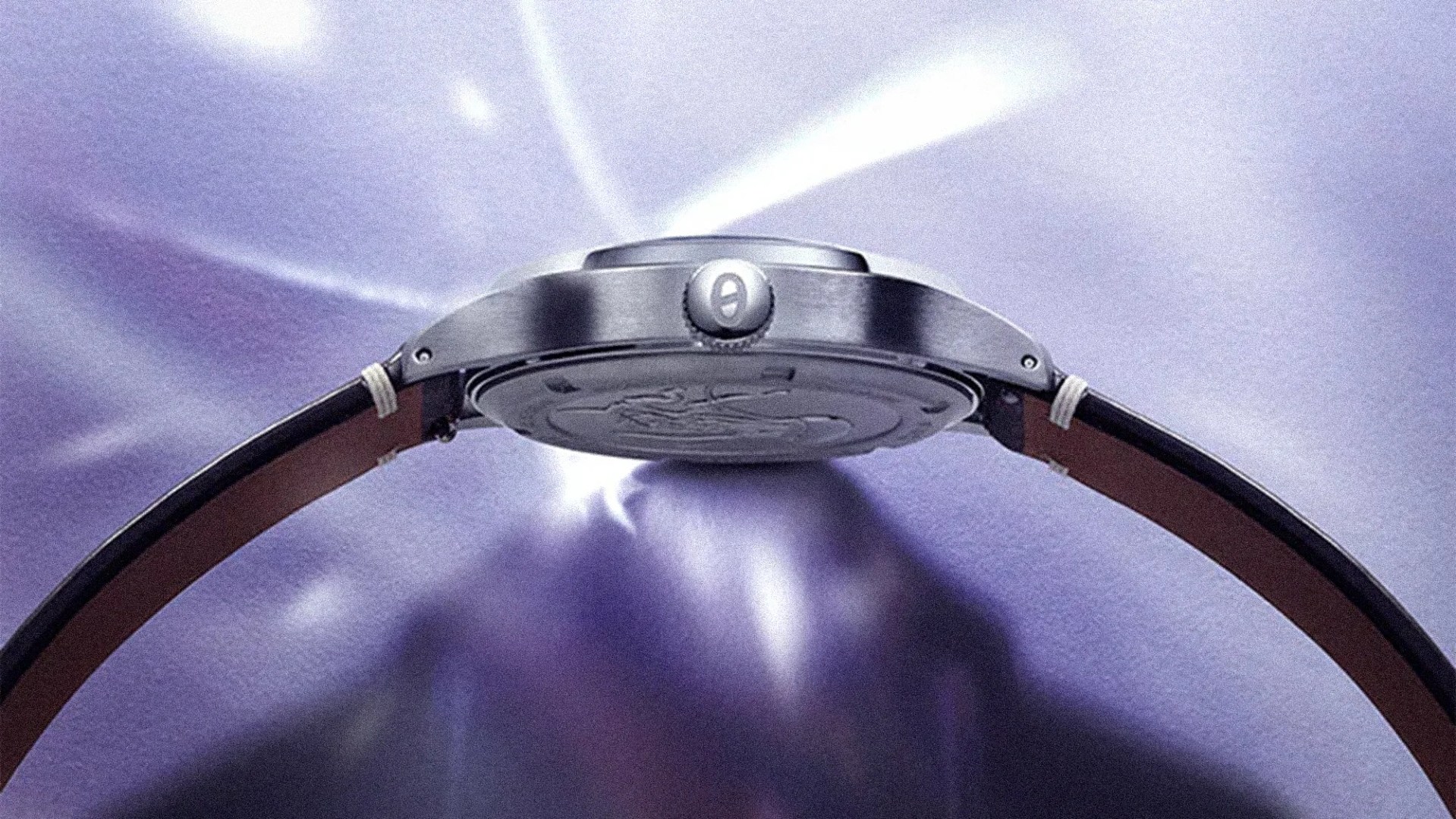 Side view of a silver wristwatch with a brown leather strap on a purple satin background.