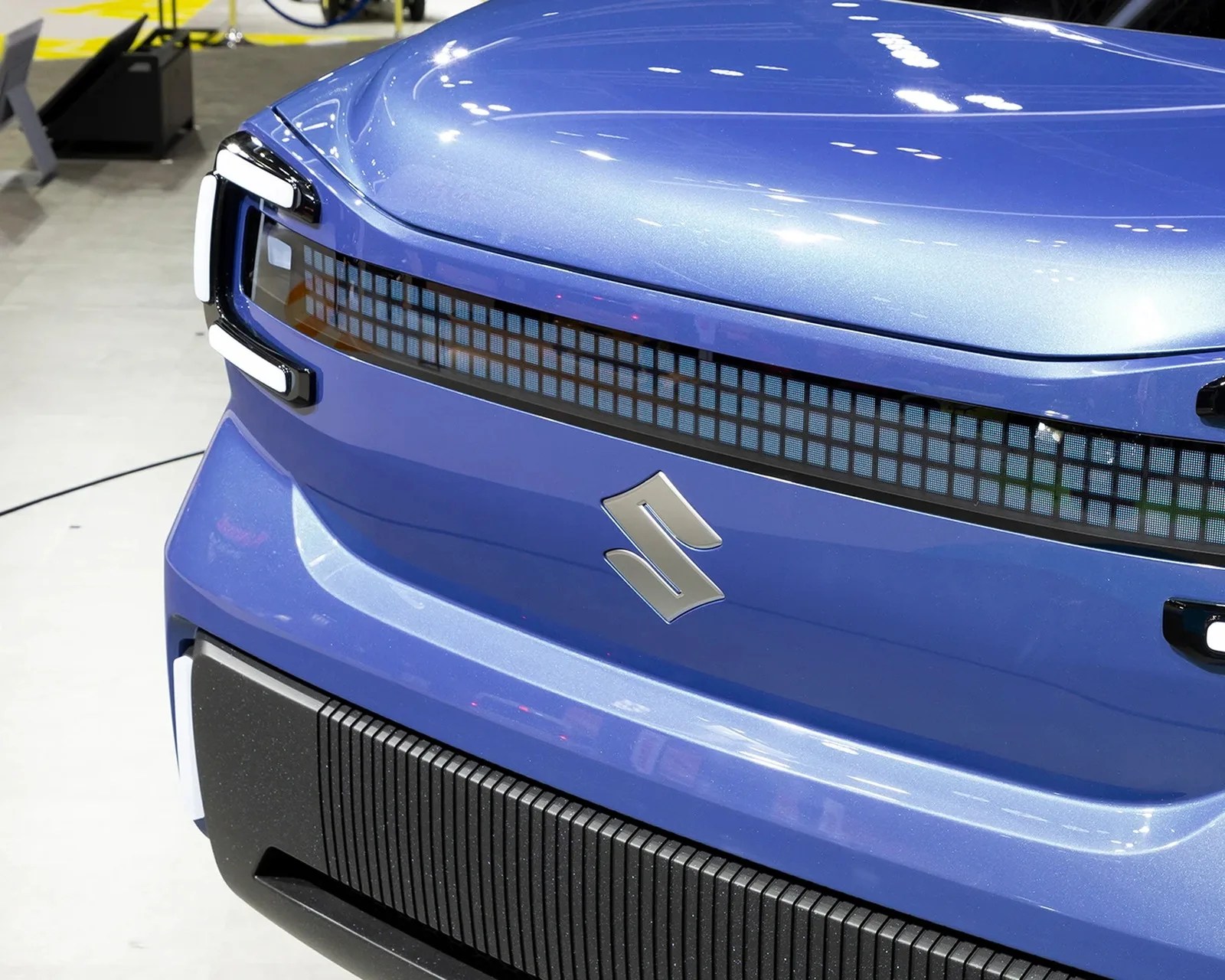 Front view of a blue Suzuki car with a pixelated LED grille and illuminated C-shaped headlights.