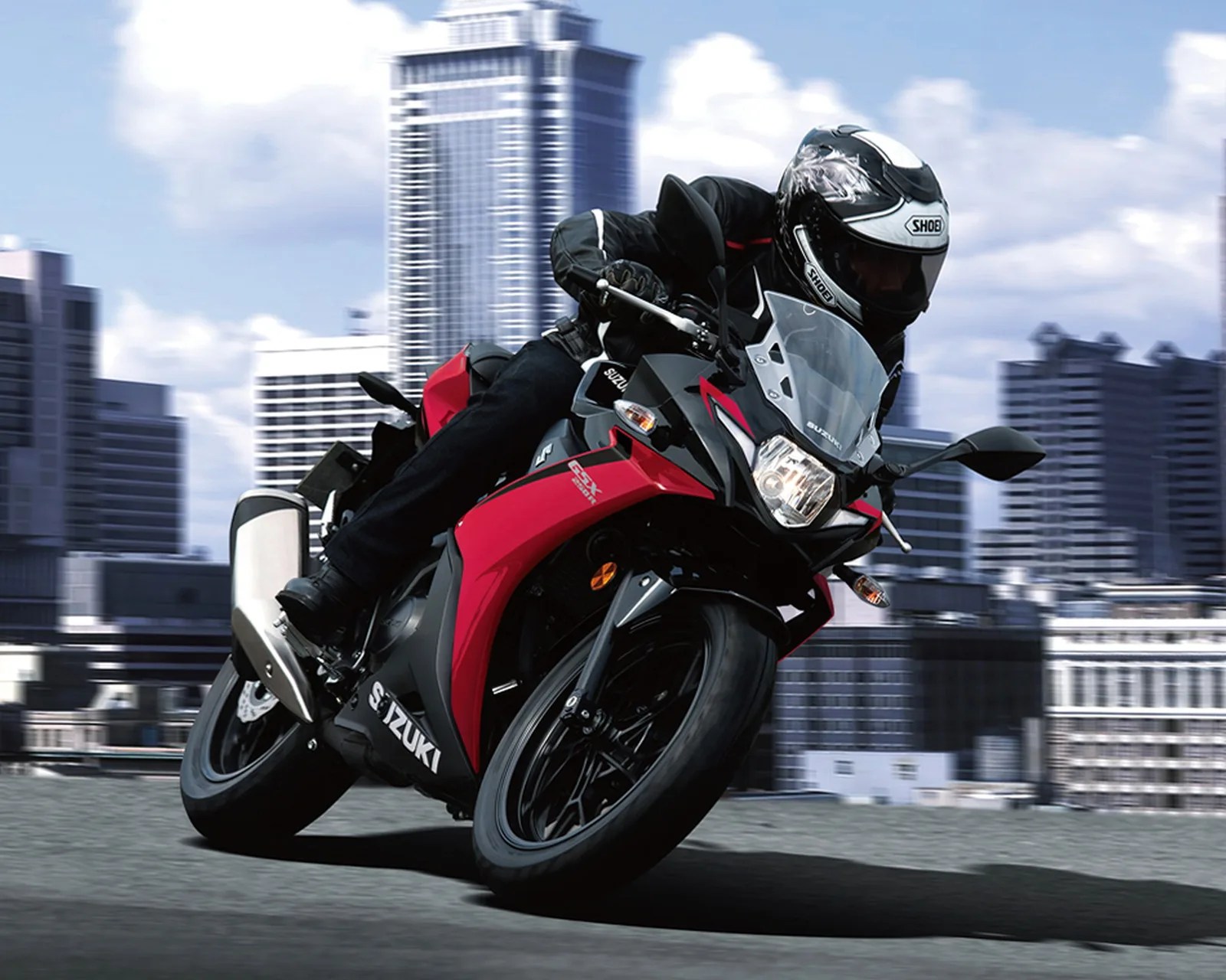Red and black Suzuki GSX motorcycle leaning into a turn on a city street with a rider wearing a black and white helmet.