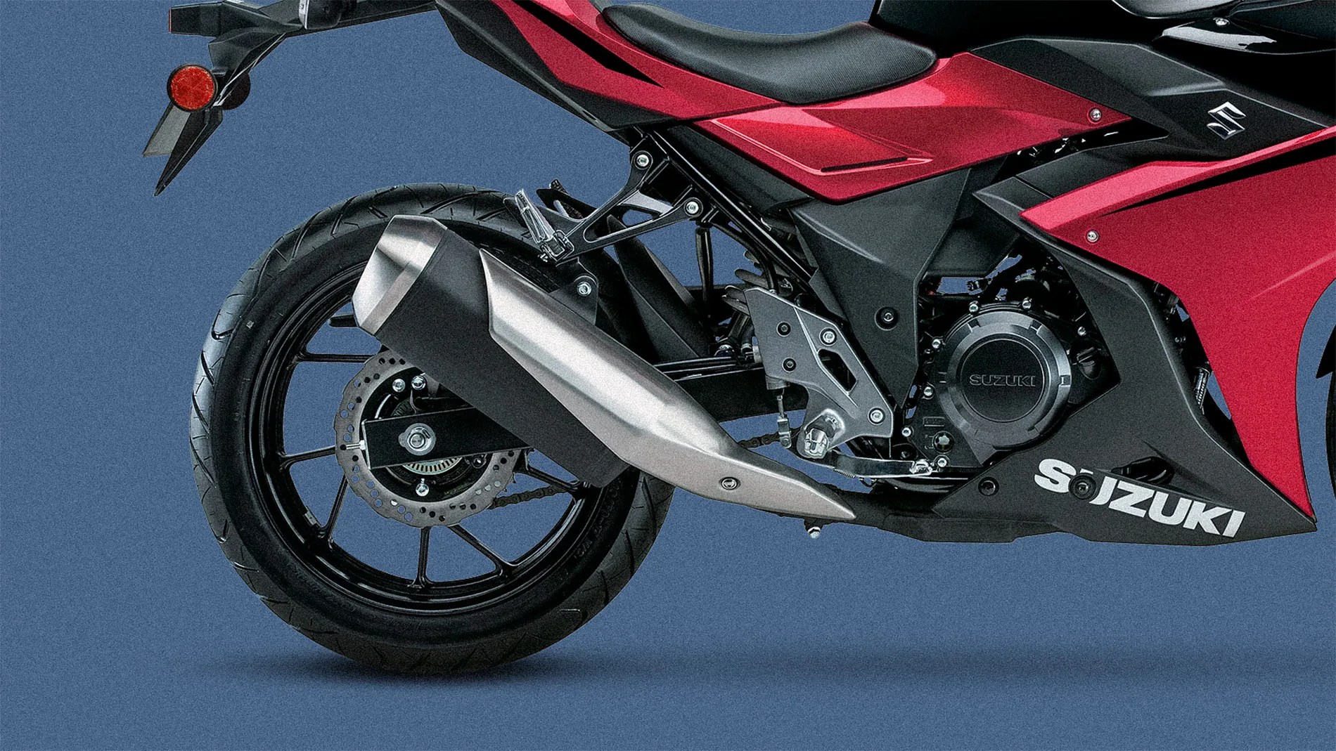 Rear section of a red and black Suzuki motorcycle showing the rear wheel, exhaust, and part of the engine.