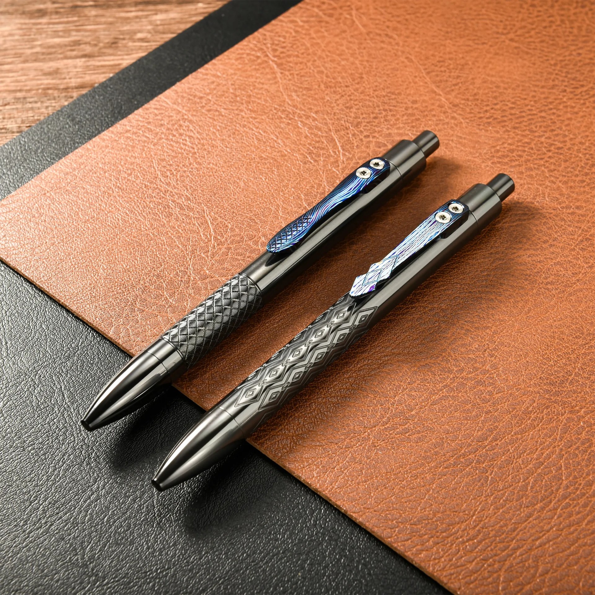 Two black metal pens with textured grips and blue patterned clips on a brown leather surface.