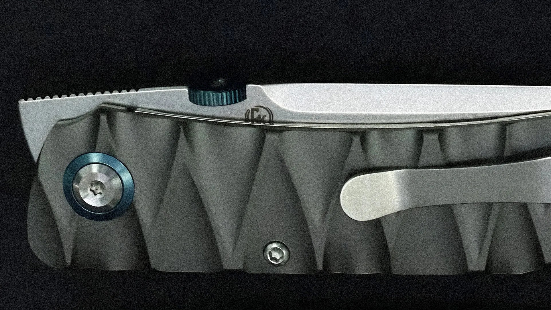 Close-up of a textured gray folding knife handle with blue screws and a silver pocket clip.
