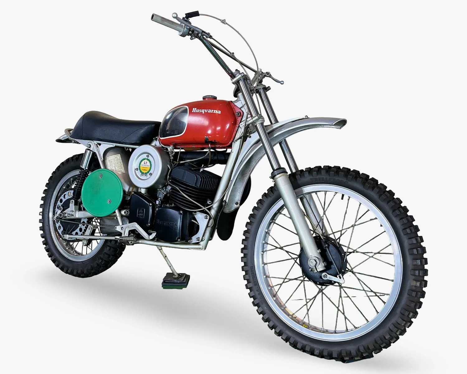 Vintage Husqvarna dirt bike with red fuel tank, black seat, and knobby tires on a white background.