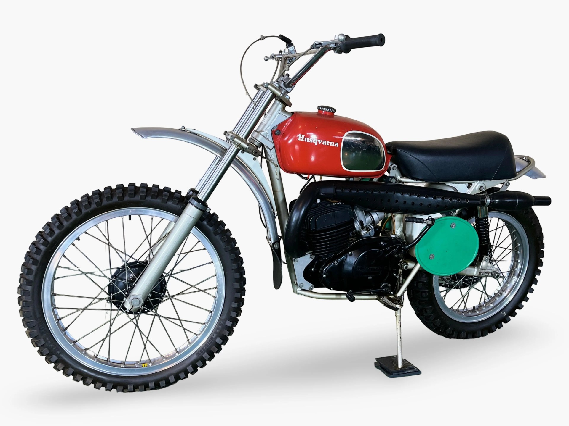 Vintage Husqvarna dirt bike with red fuel tank, black seat, and knobby tires on a white background.