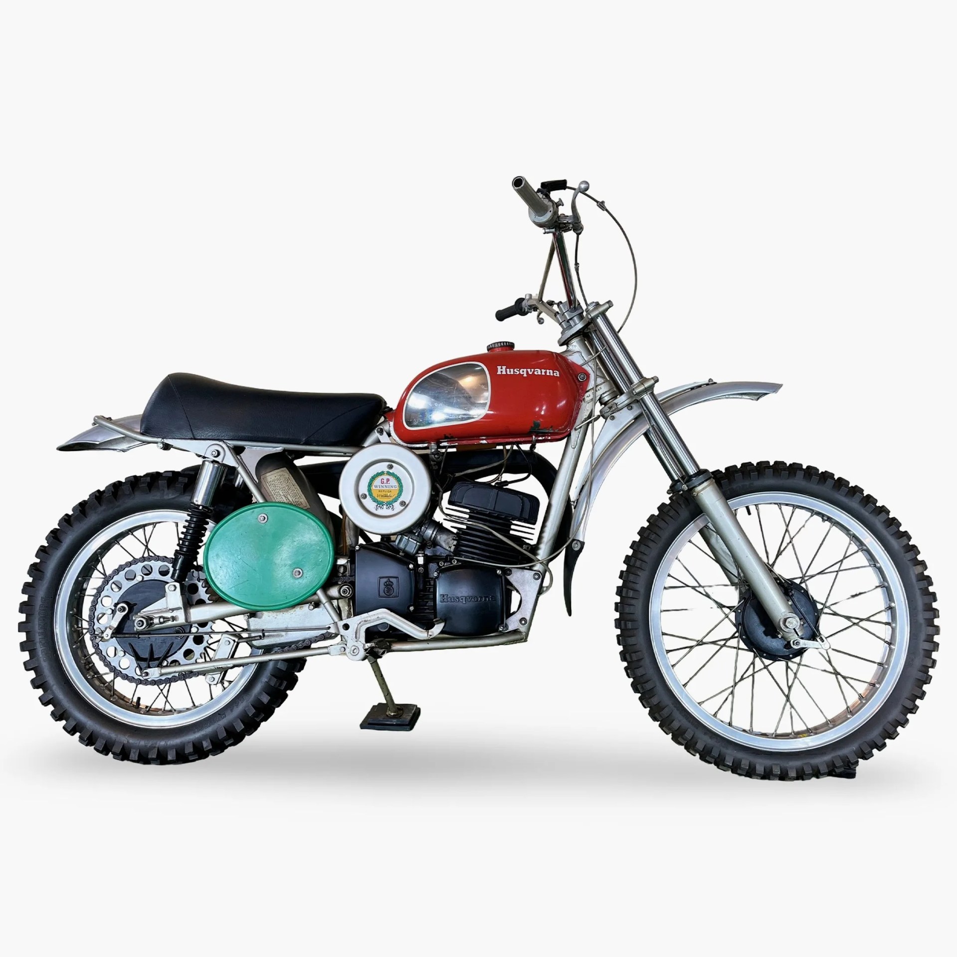 Vintage Husqvarna dirt bike with red fuel tank, black seat, and knobby tires on a white background.