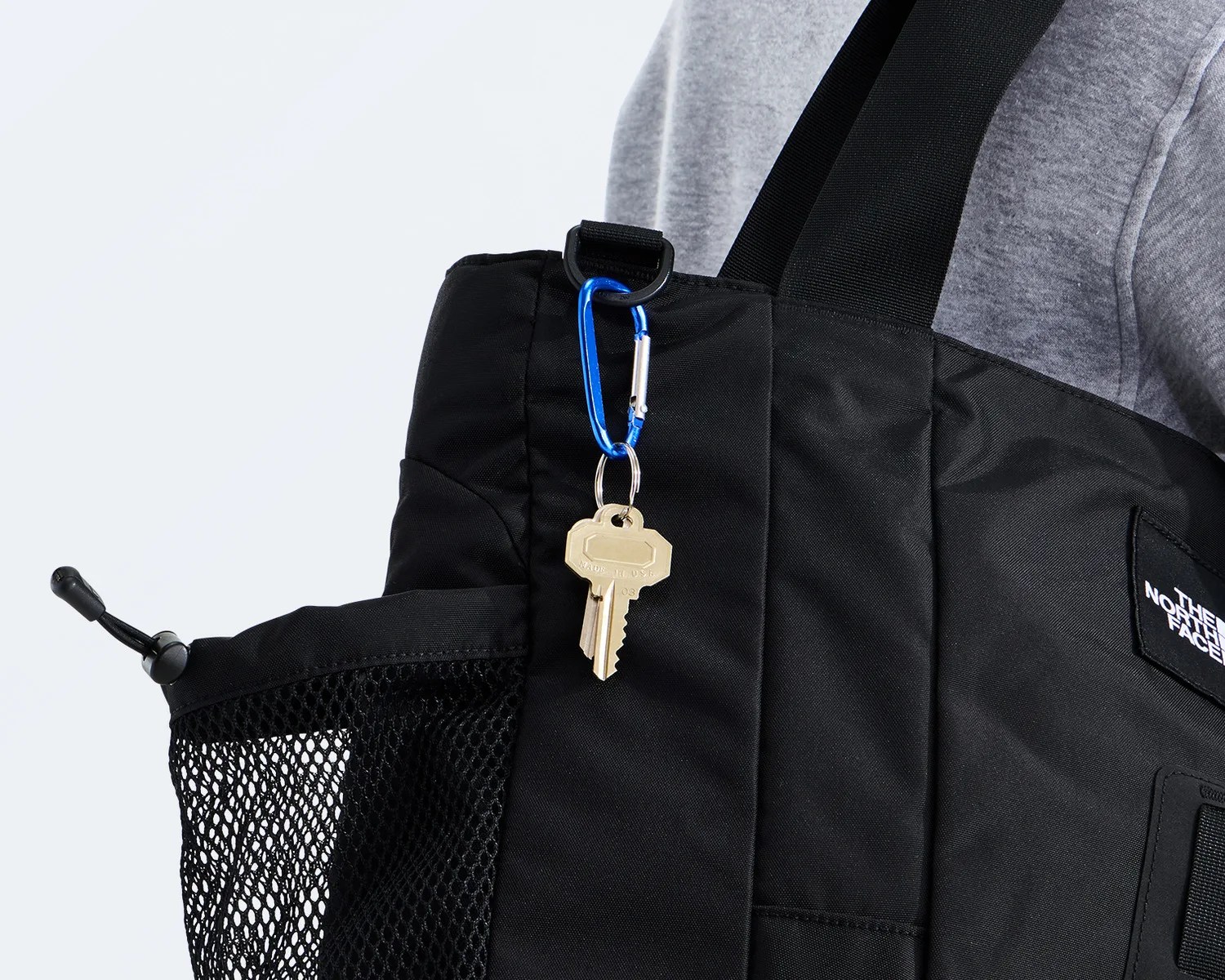 Black The North Face tote bag with mesh side pocket and blue carabiner holding two keys.