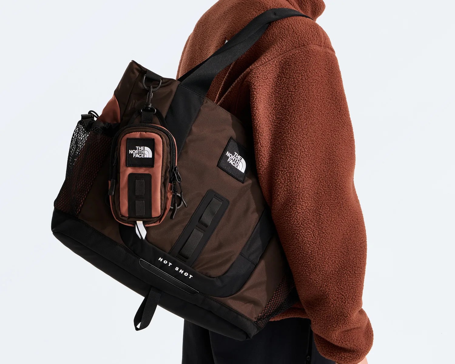 Brown and black The North Face tote bag with a small attached pouch worn over a rust-colored fleece jacket.