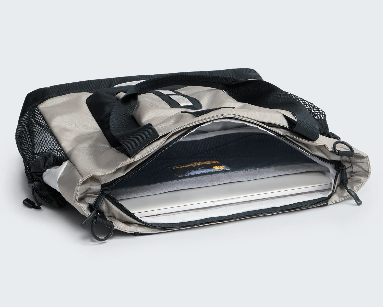Beige and black laptop bag with mesh side pockets and a partially open zipper showing a laptop inside.