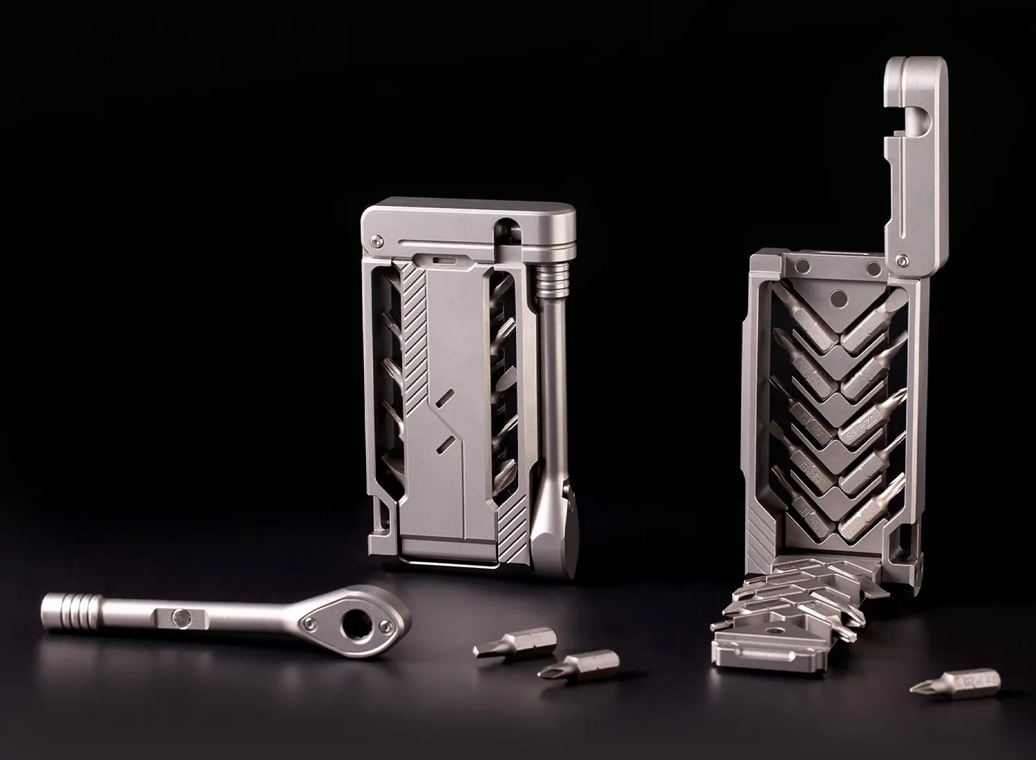 Compact silver multi-bit screwdriver set with bits stored inside two metal cases and a detachable ratchet handle on a black surface.