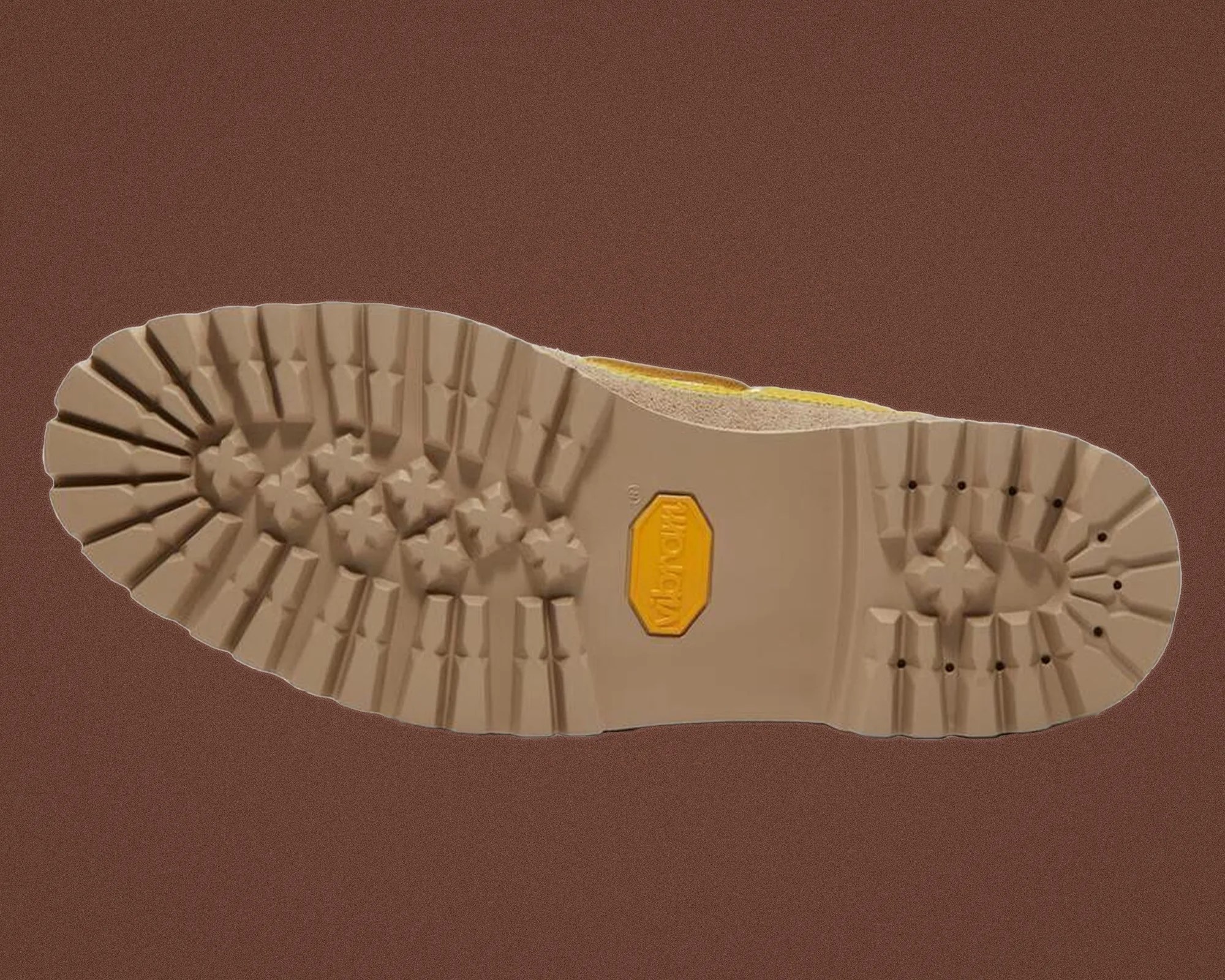 Beige rubber shoe sole with deep treads and a yellow Vibram logo in the center.