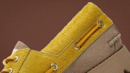 Close-up of a yellow and beige suede shoe with yellow laces threaded through metal eyelets.