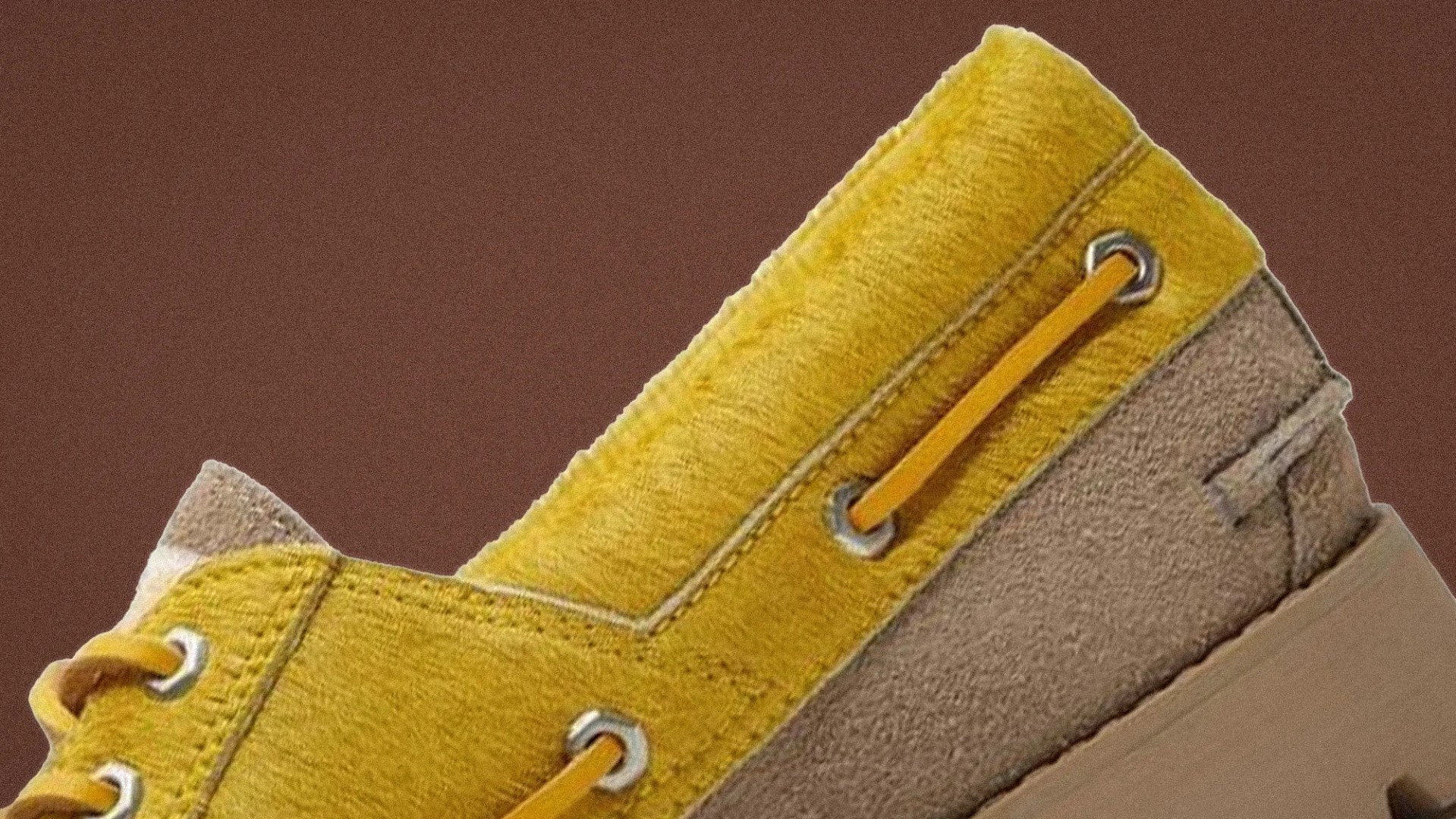 Close-up of a yellow and beige suede shoe with yellow laces threaded through metal eyelets.