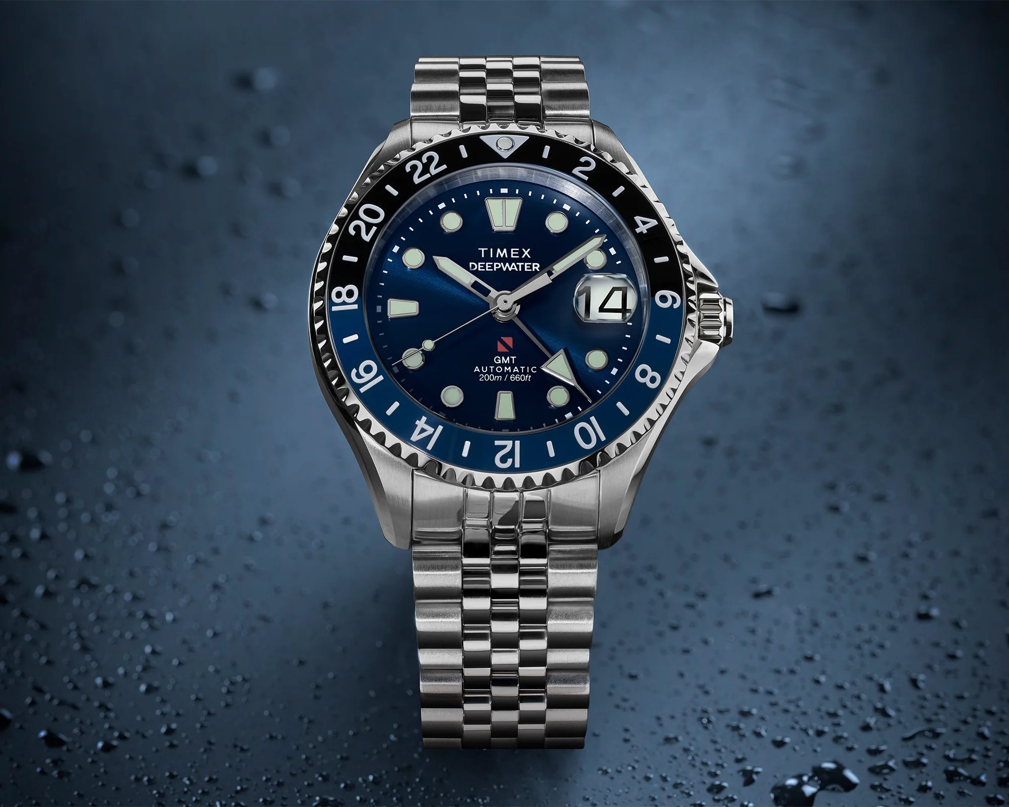 Stainless steel Timex Deepwater GMT automatic watch with blue dial and black-blue bezel on a wet surface.