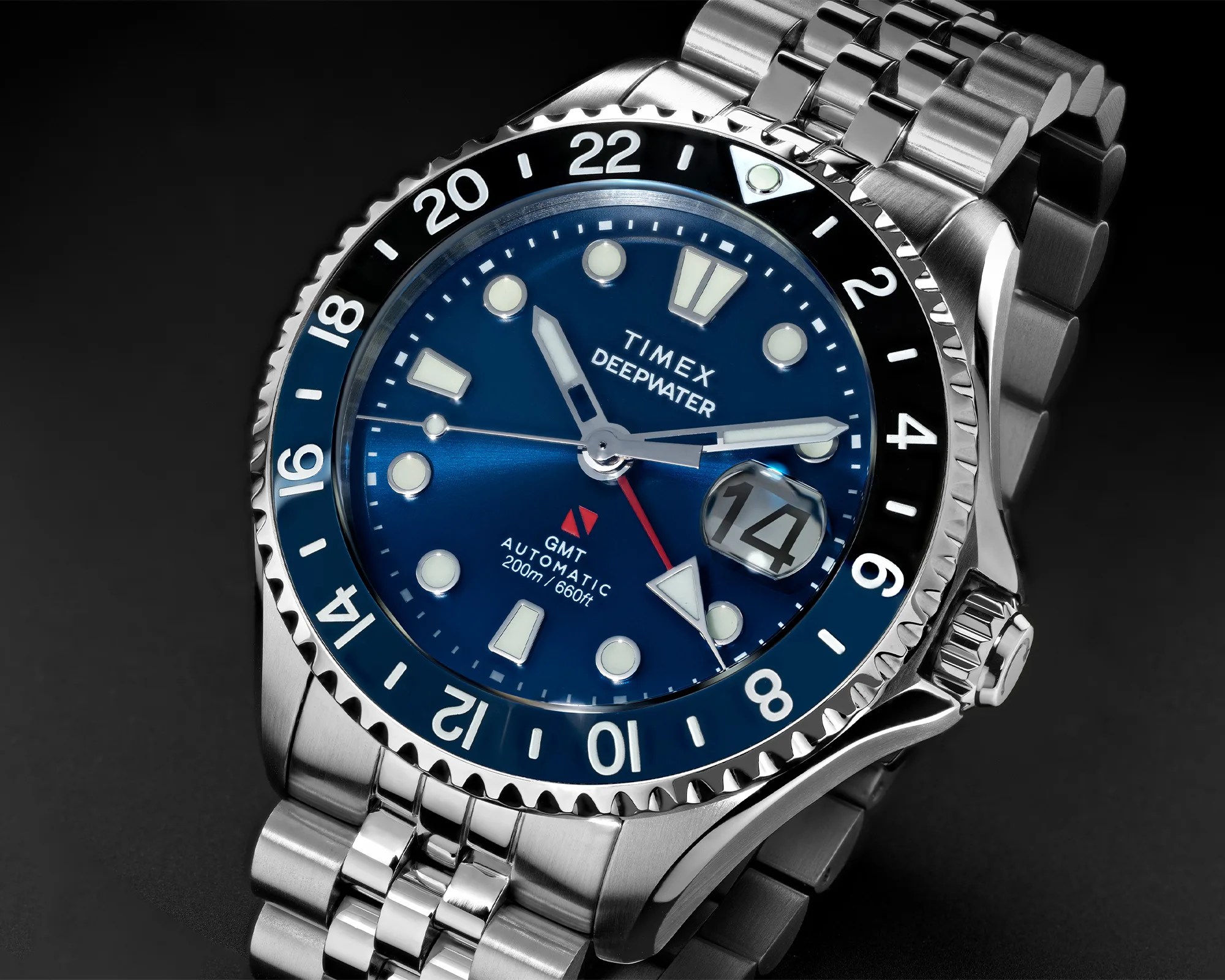 Close-up of a Timex Deepwater GMT automatic watch with blue dial, date window, and stainless steel bracelet.