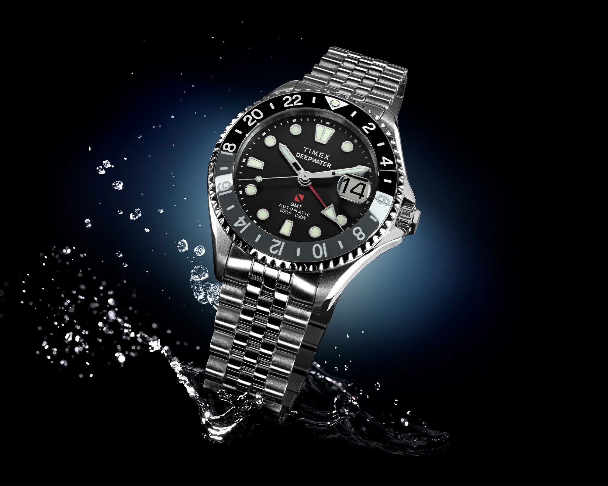 Stainless steel Timex Deepwater GMT watch with black dial and luminous markers splashing in water.
