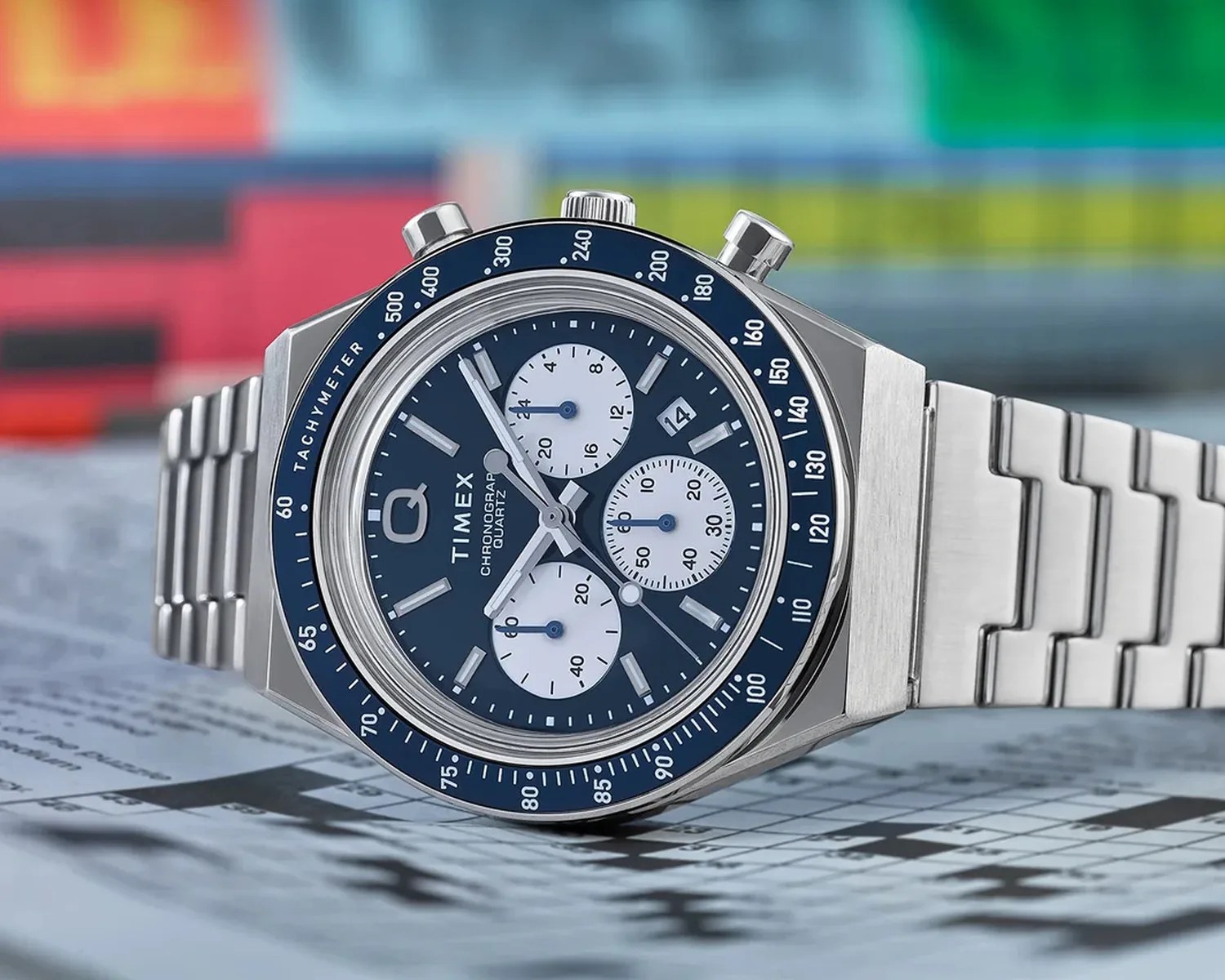 Silver stainless steel Timex chronograph watch with blue dial and three white subdials on a crossword puzzle background.