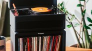 Black Tinyvinyl turntable with orange vinyl record on top of a matching black storage unit filled with vinyl records.