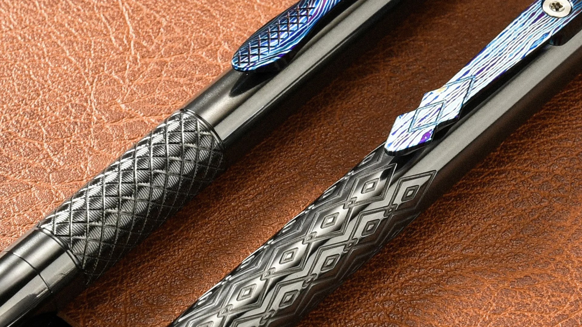Two black pens with textured diamond patterns on their barrels and blue patterned clips on a brown leather surface.