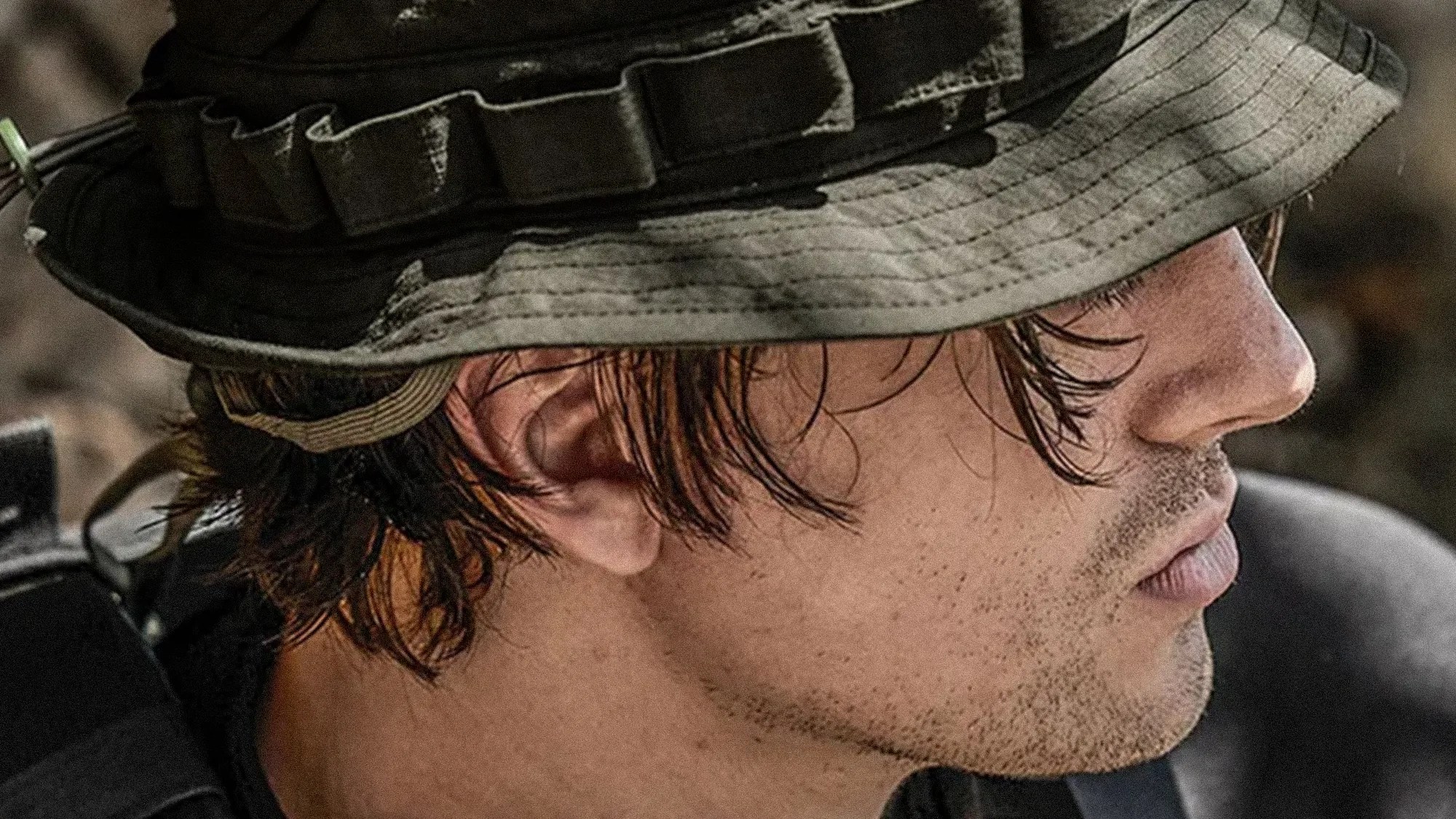 Close-up of a person wearing a green tactical boonie hat with a strap and short dark hair.