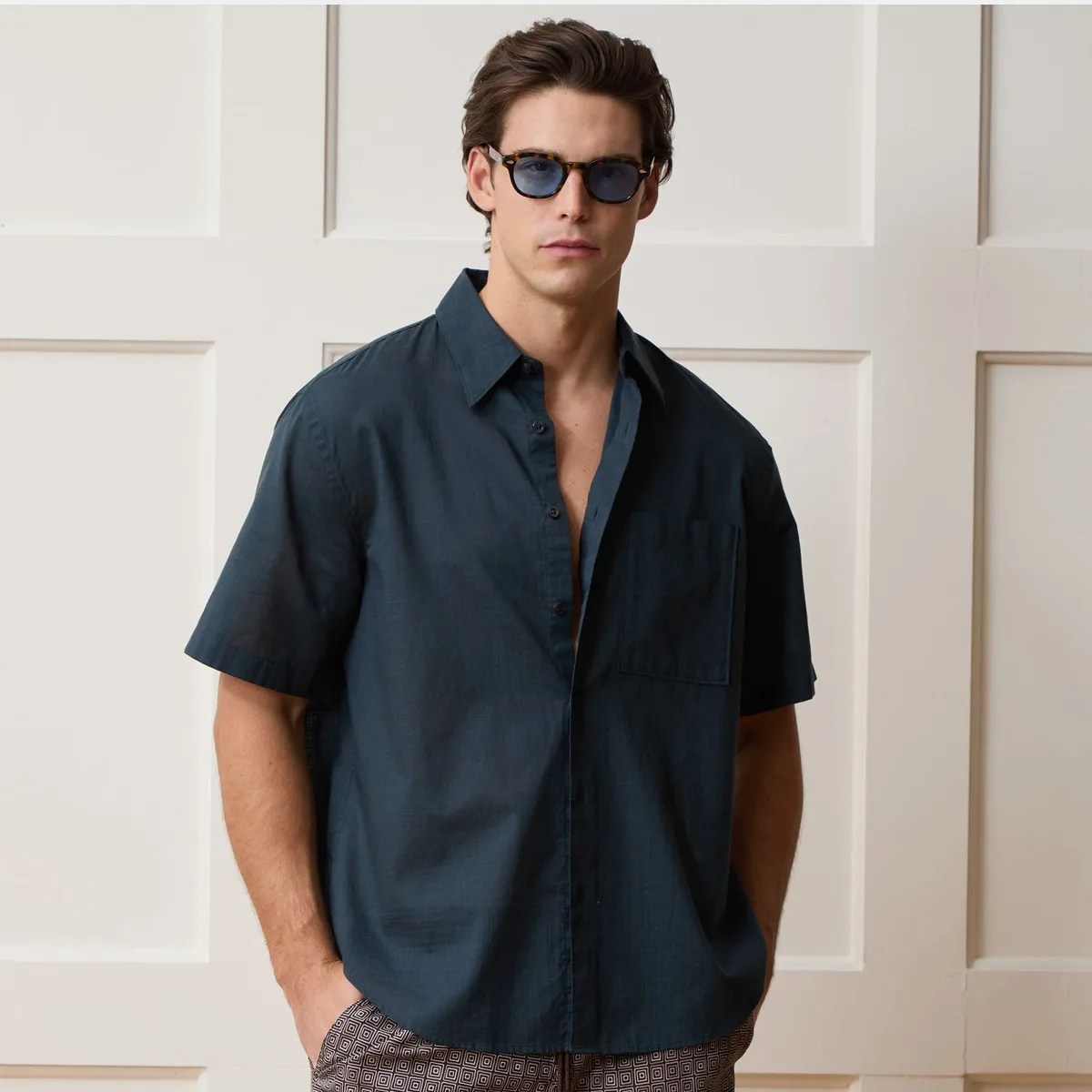 Man wearing a dark blue short-sleeve button-up shirt and tortoiseshell sunglasses.