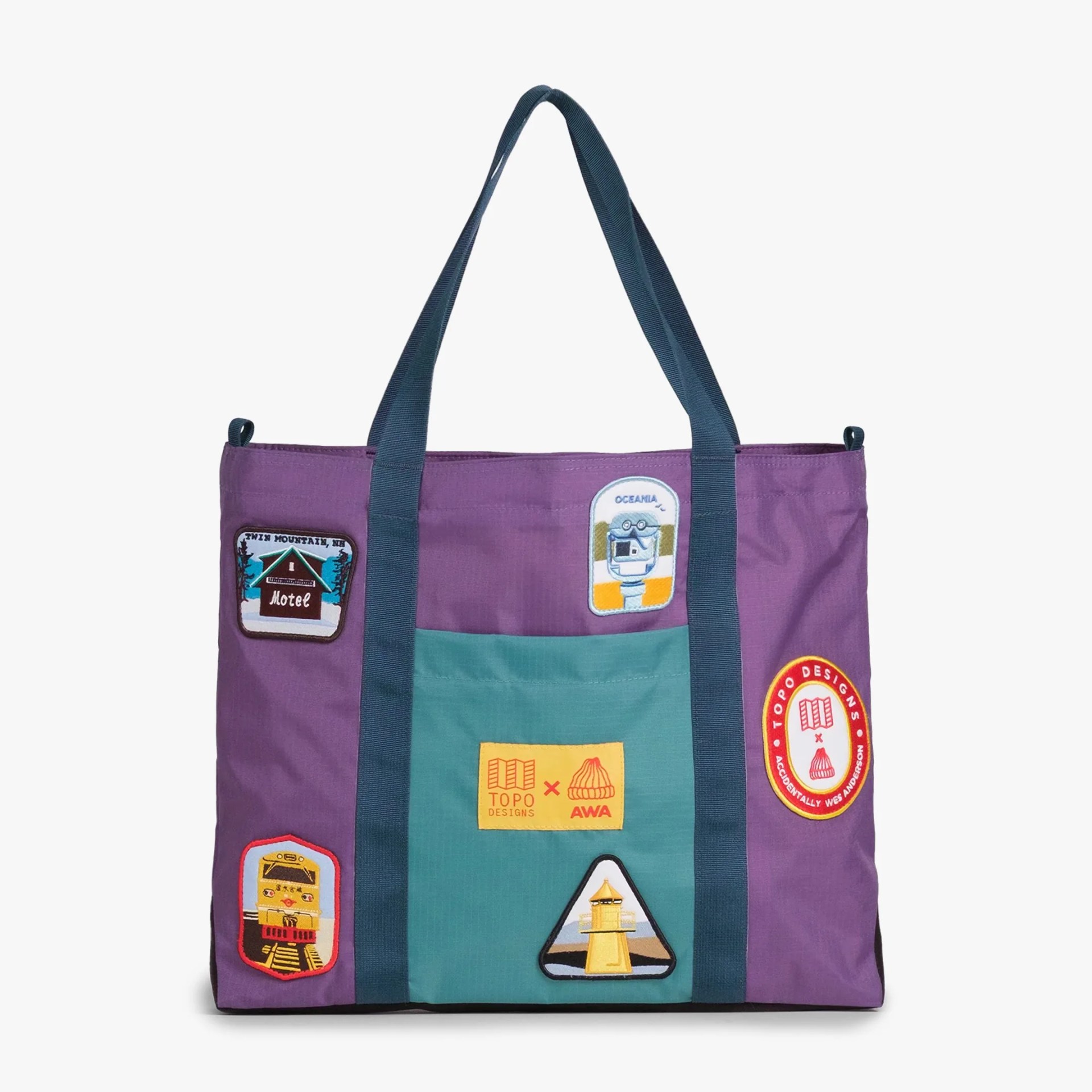 Purple and teal tote bag with dark blue handles and multiple colorful patches including a motel, train, lighthouse, and Topo Designs logos.