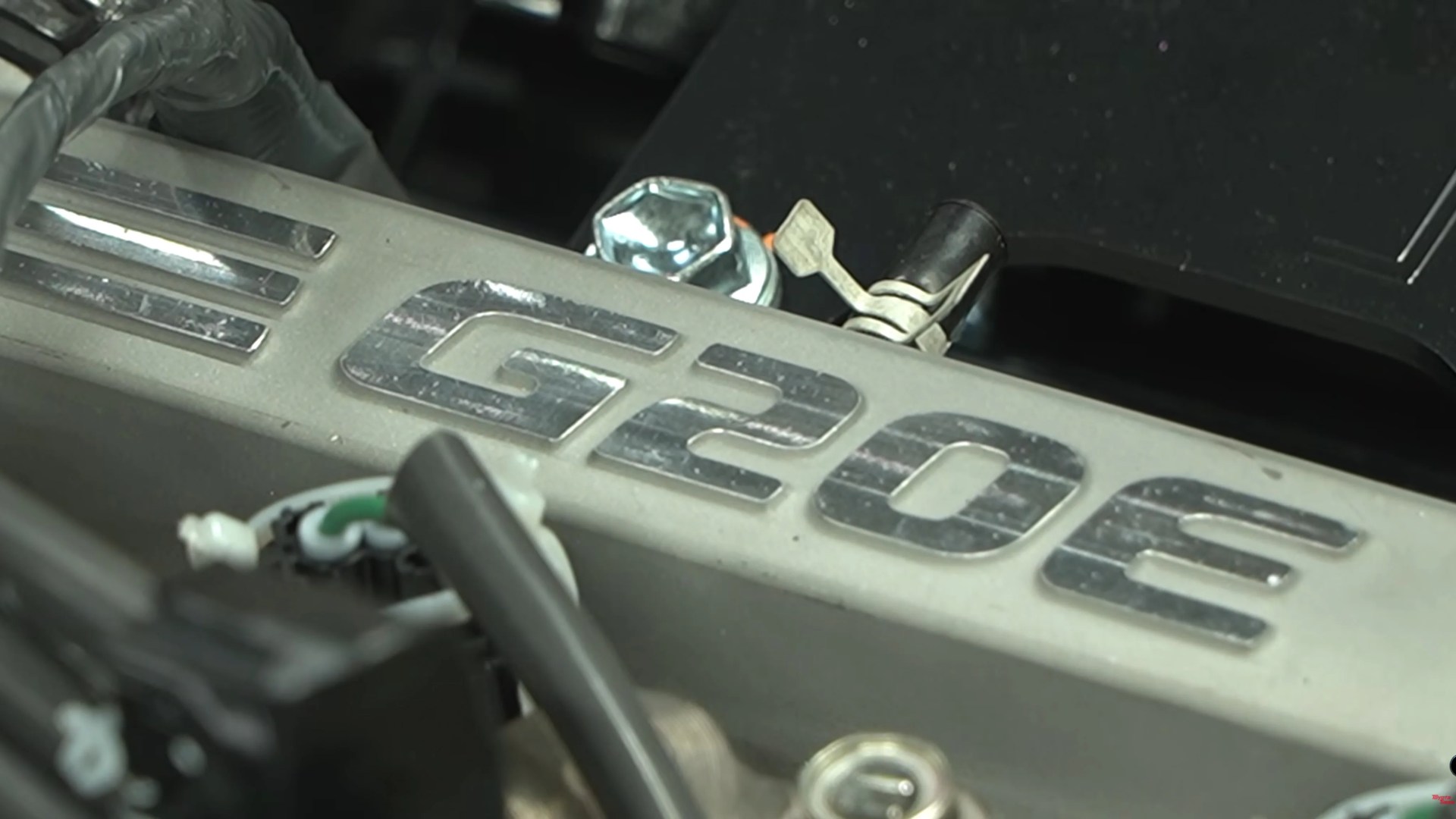 Close-up of a metallic engine part with "G20e" embossed on it, surrounded by bolts and wires.