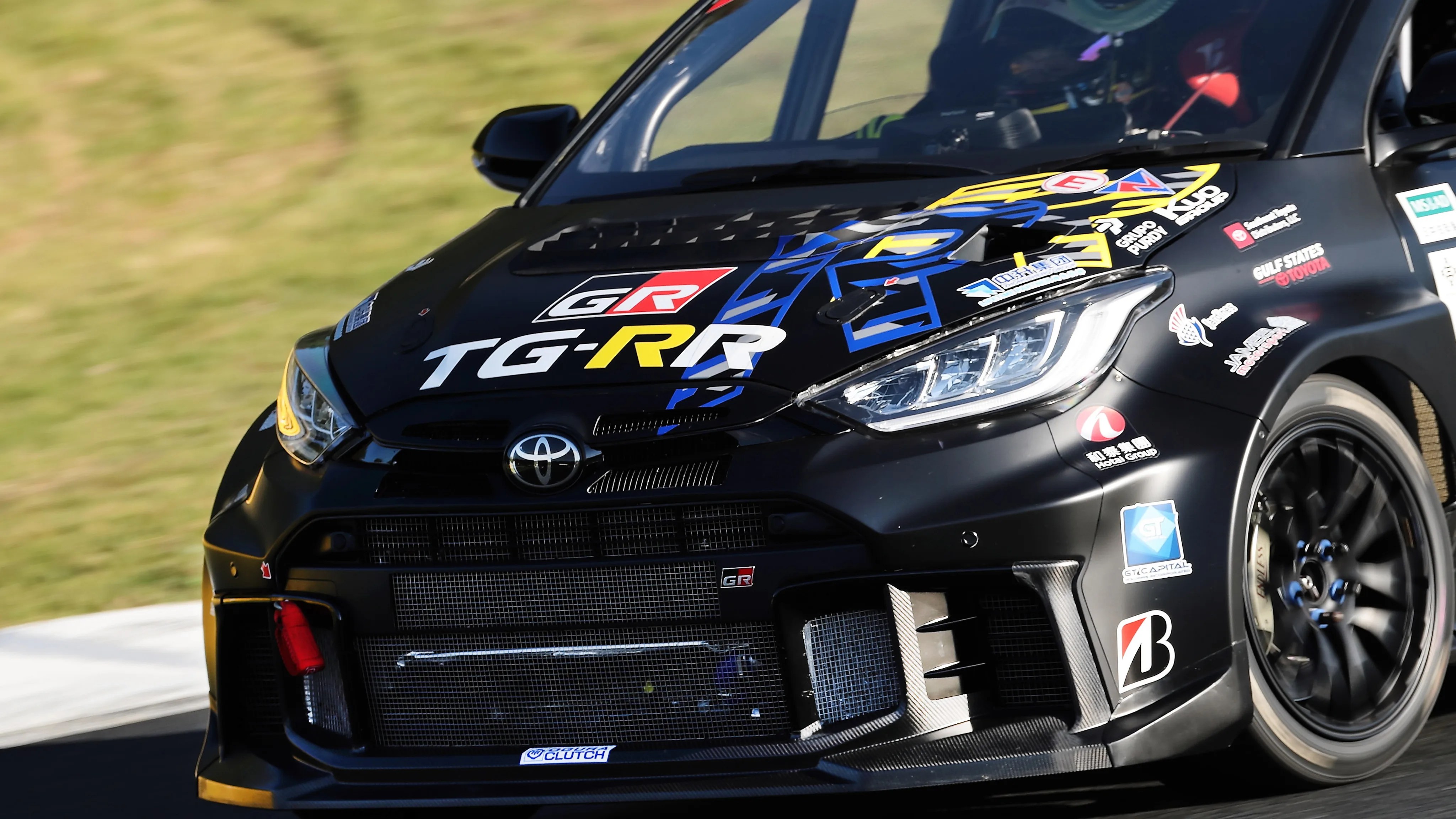 Front view of a black Toyota GR racing car with sponsor decals and blue and yellow graphics on the hood.