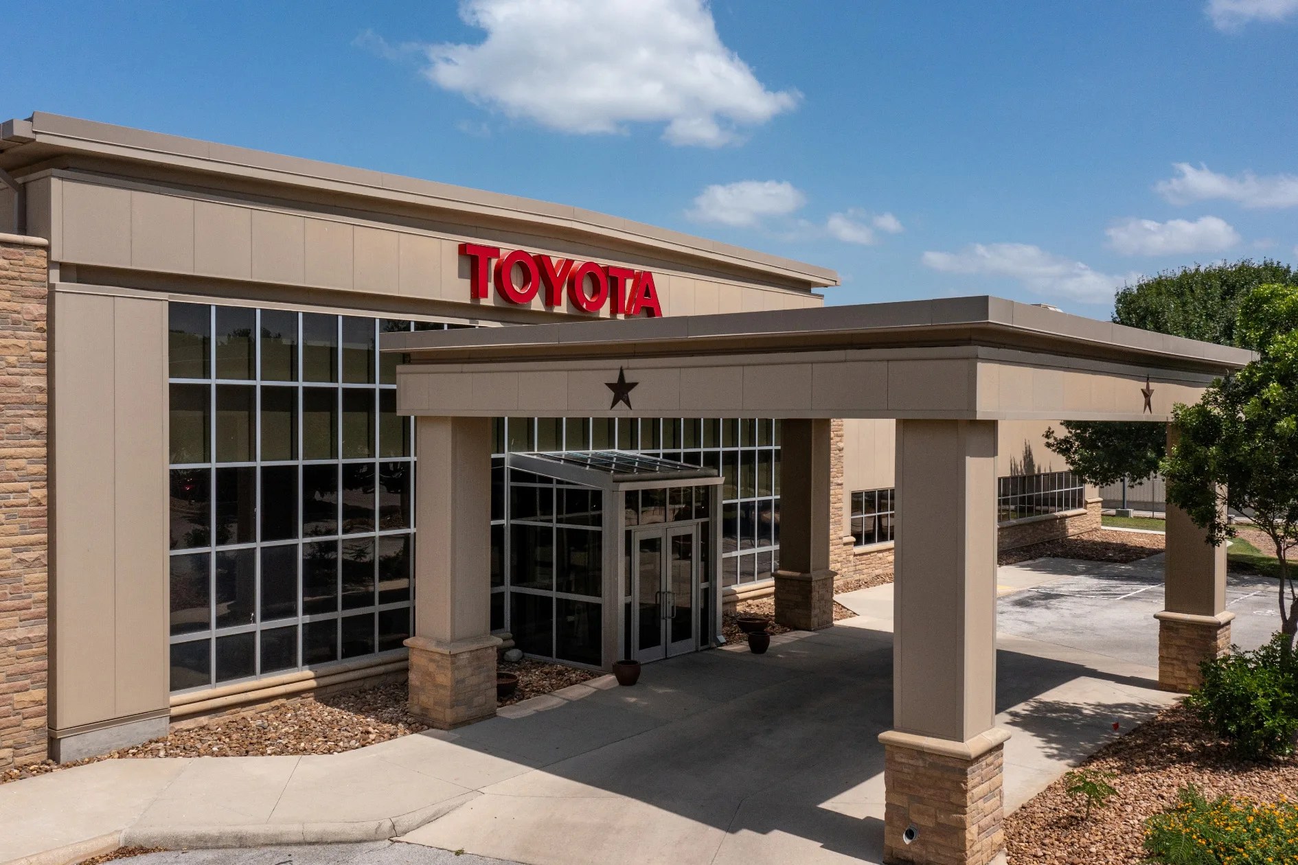 Beige Toyota dealership building with large windows and covered entrance under blue sky.