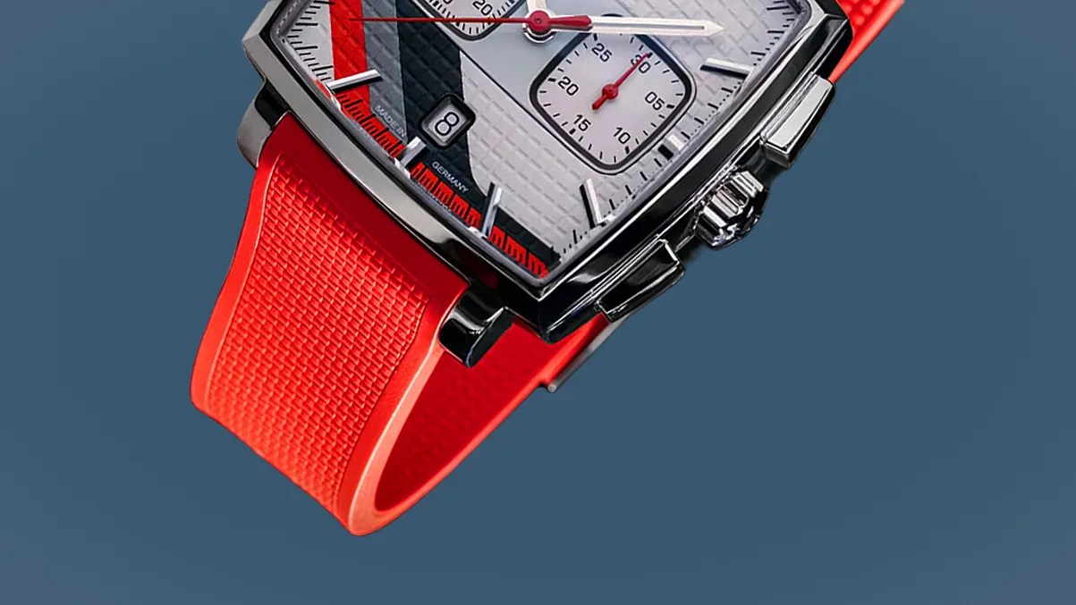 Square silver watch with white dial, red and black accents, and textured bright red rubber strap.