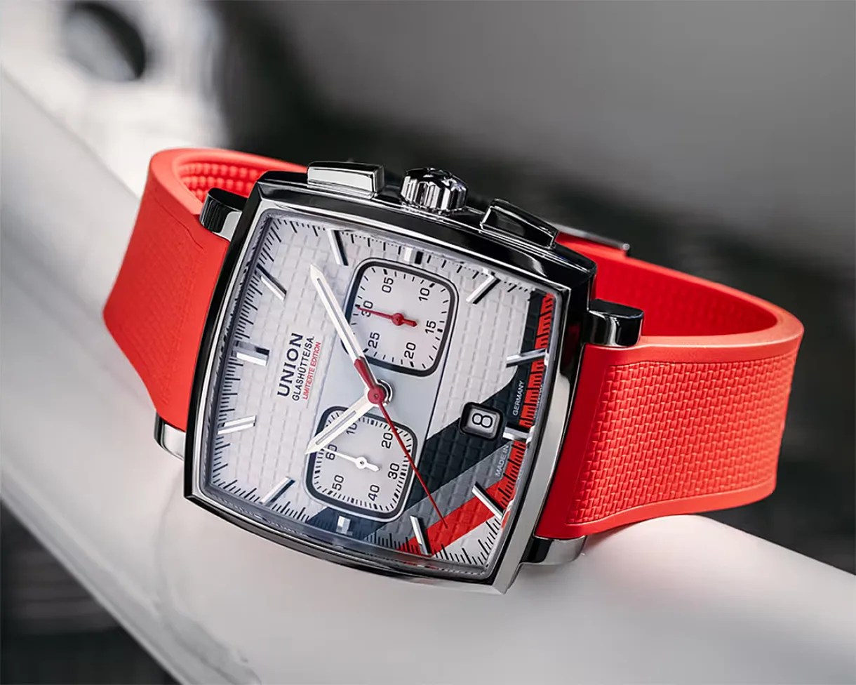 Square silver watch with white textured dial, red and black accents, and a red textured rubber strap.