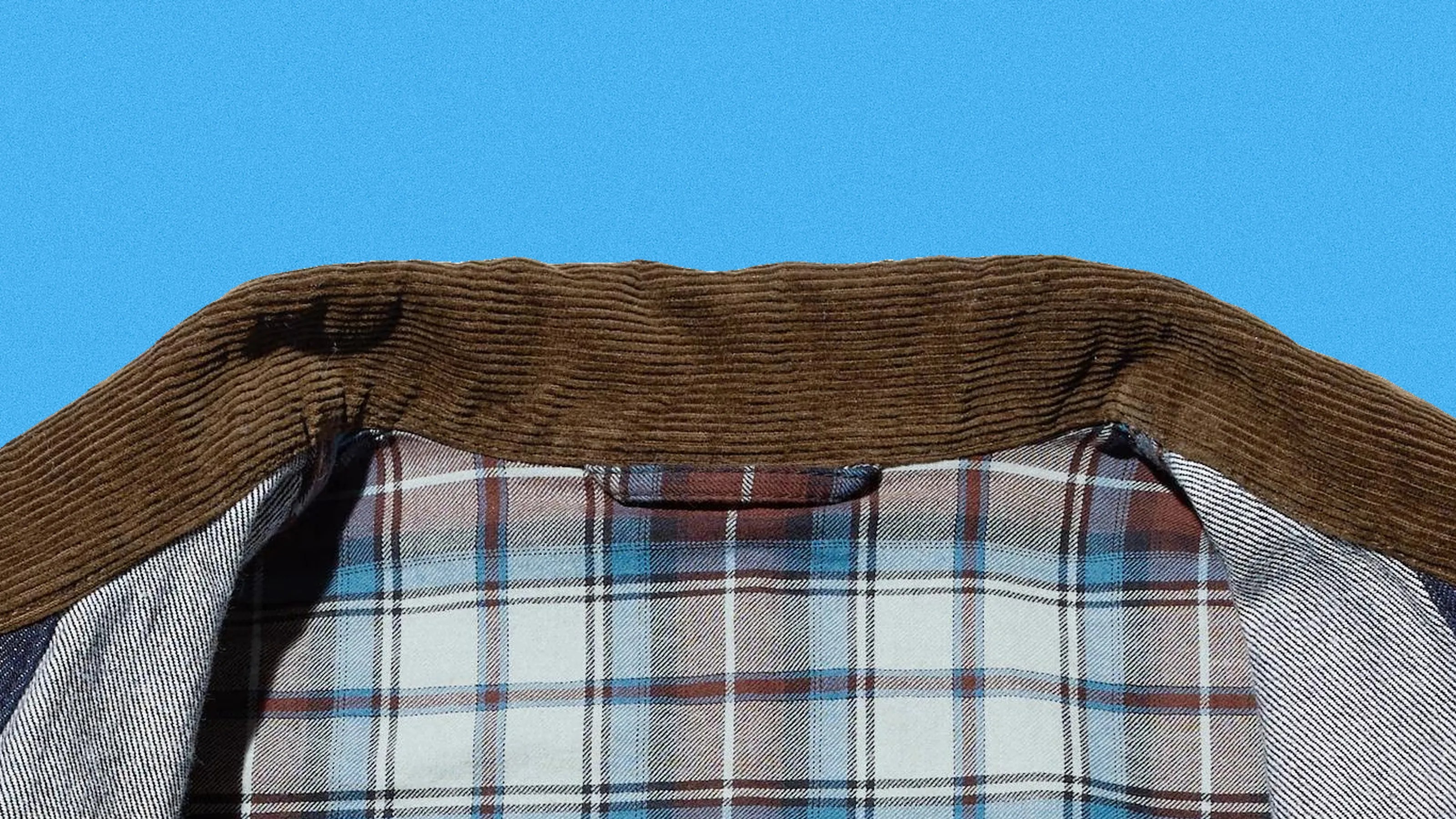 Brown corduroy collar on a plaid shirt with blue, white, and brown checks against a blue background.