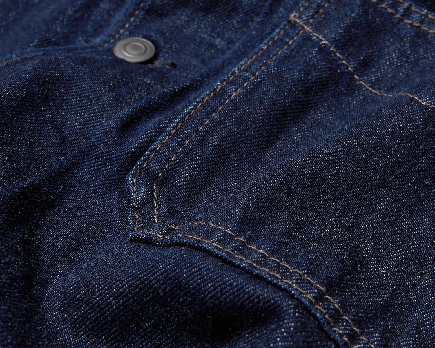 Close-up of dark blue denim fabric with visible stitching and a metal button.