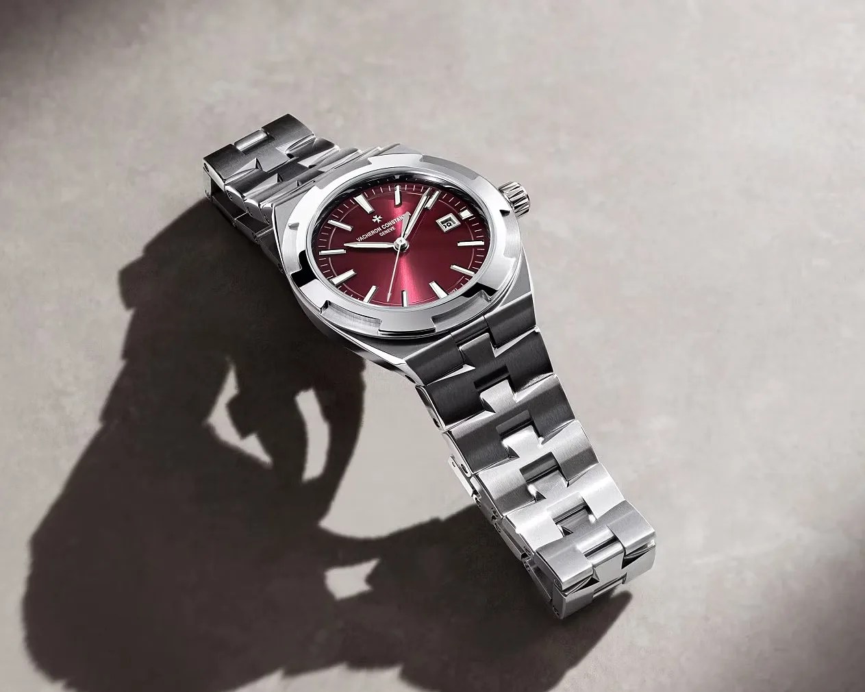 Silver stainless steel wristwatch with a burgundy dial and date display on a light gray surface.