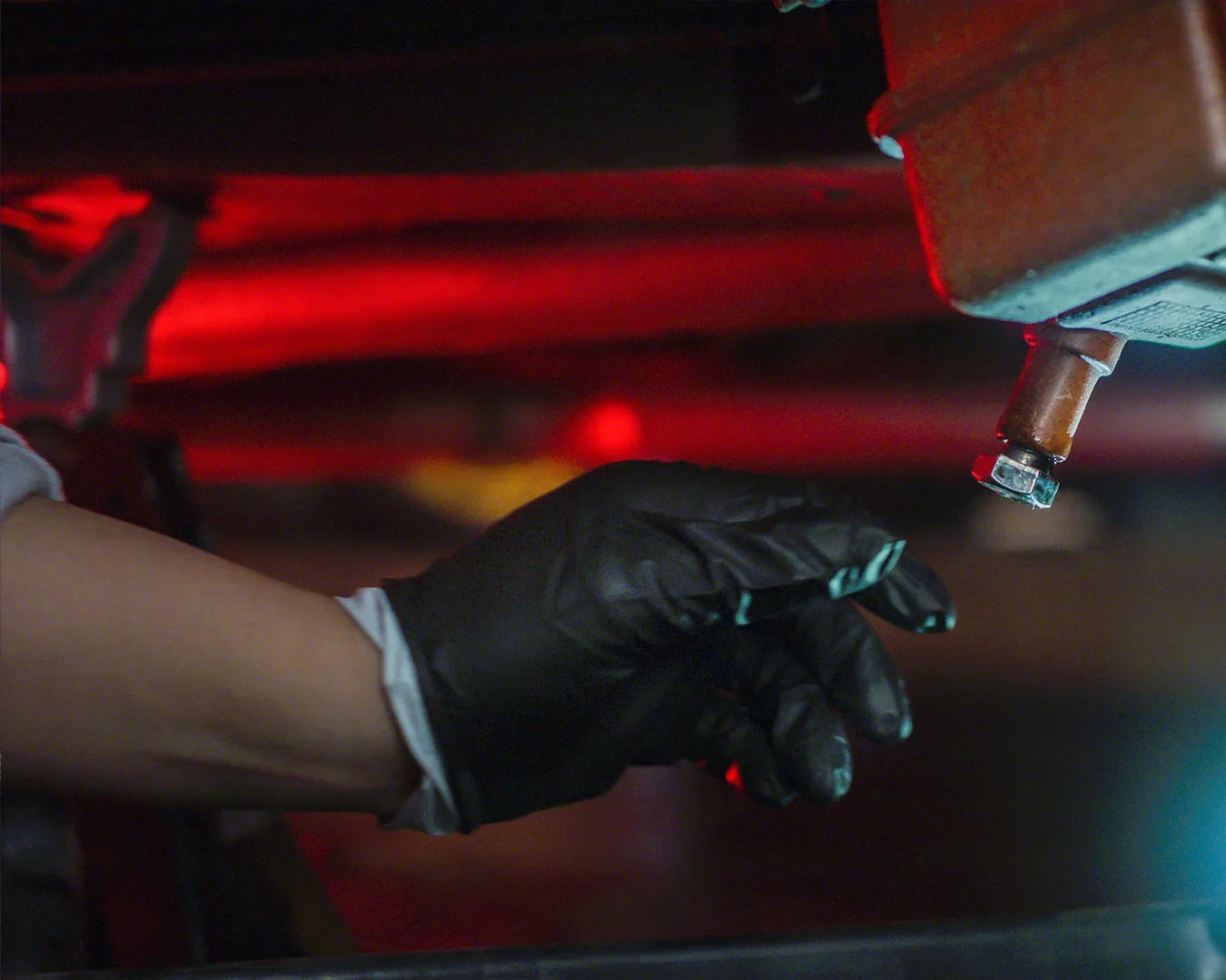 Hand wearing a black glove reaching toward a metal valve with a red light in the background.