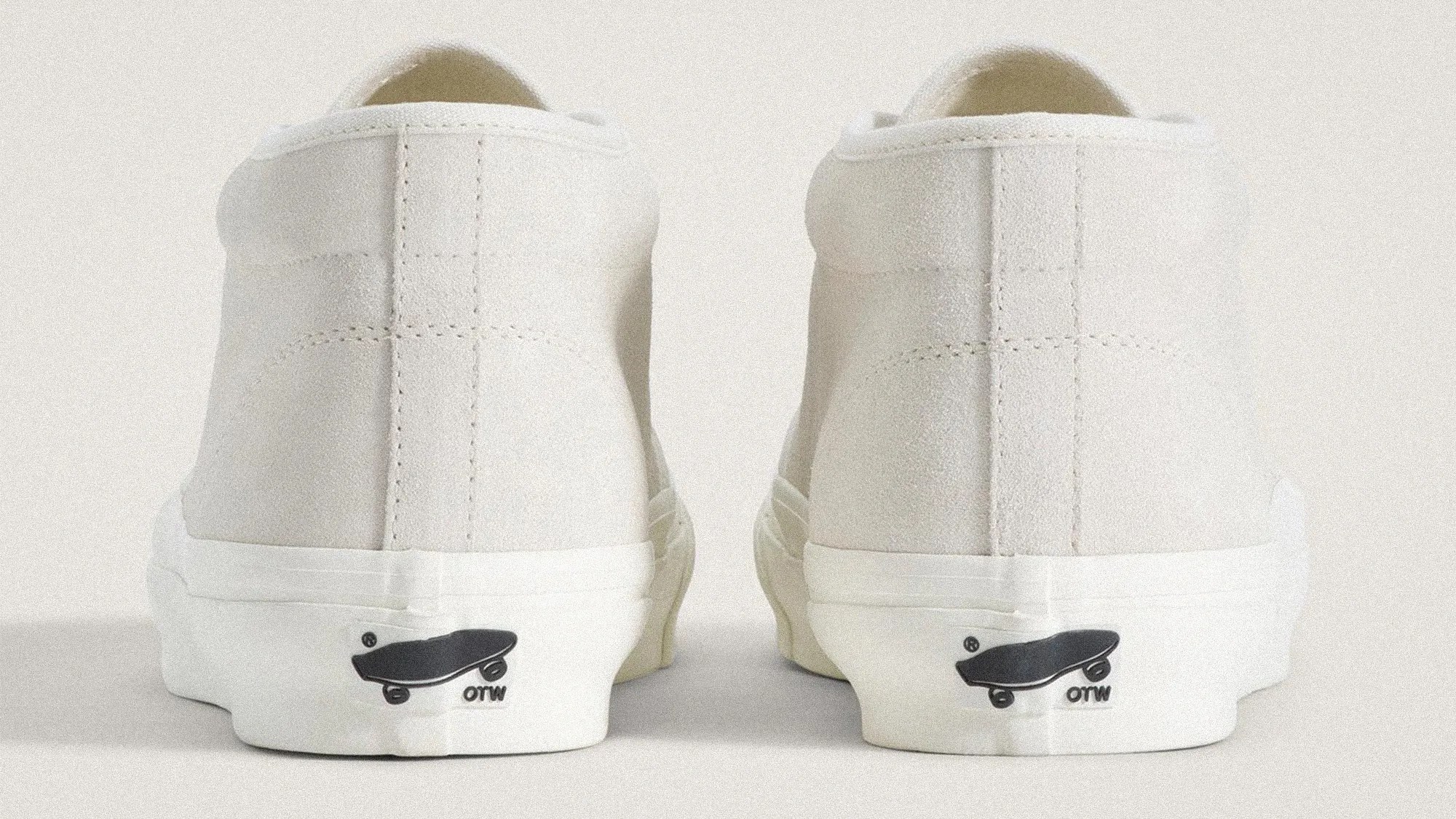 Pair of off-white suede sneakers shown from the back with black skateboard logo on the white rubber sole.