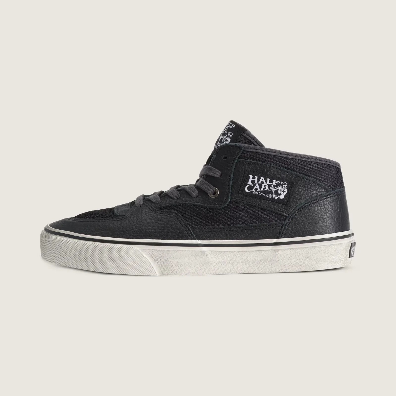 Black Vans Half Cab mid-top sneaker with textured leather and mesh upper, white logo patch, and white rubber sole.