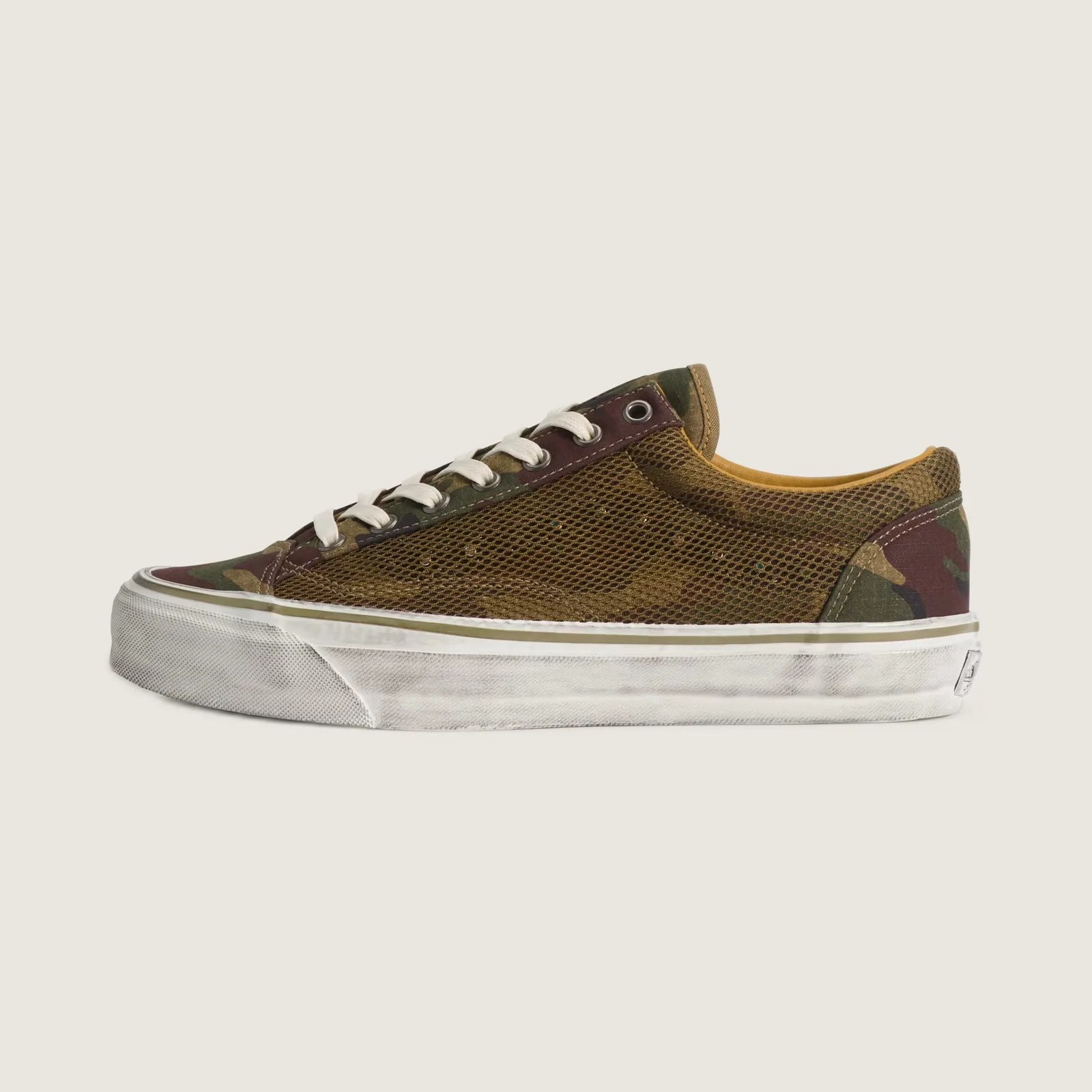 Low-top sneaker with camouflage and mesh upper, white laces, and worn white rubber sole.