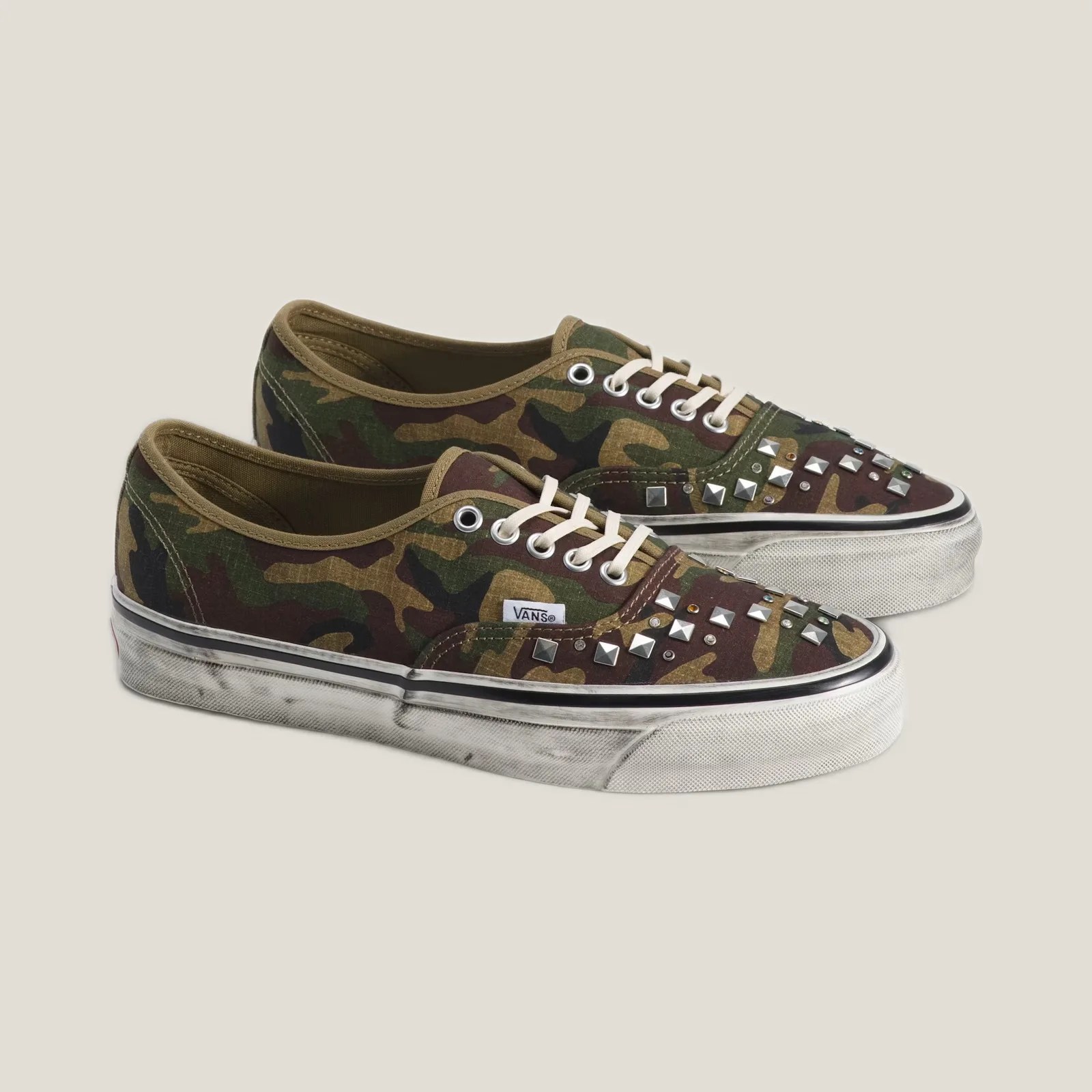Pair of camo-patterned Vans sneakers with white laces and silver studs on the toe area.