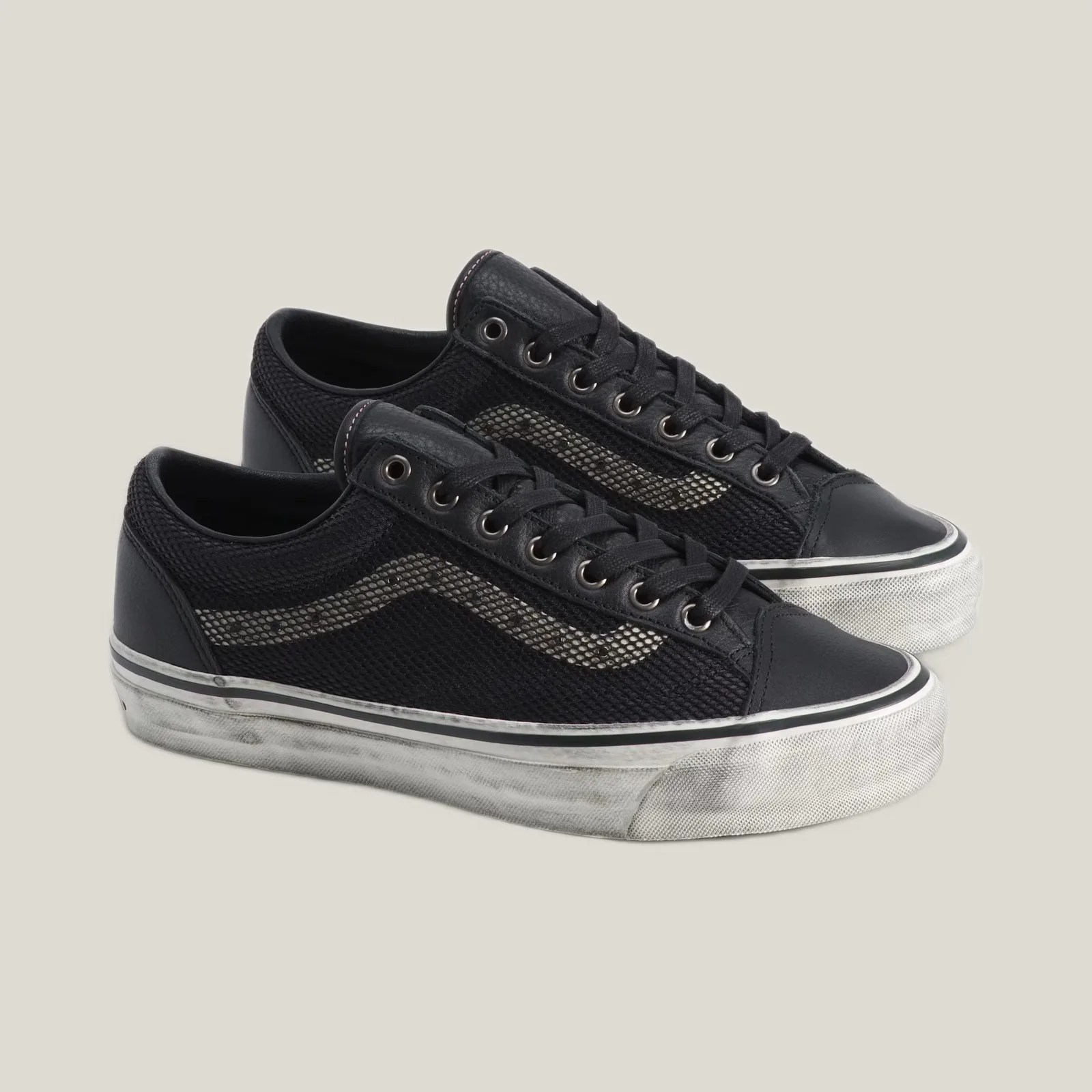 Pair of black low-top mesh and leather sneakers with white rubber soles and a white wave stripe on the sides.