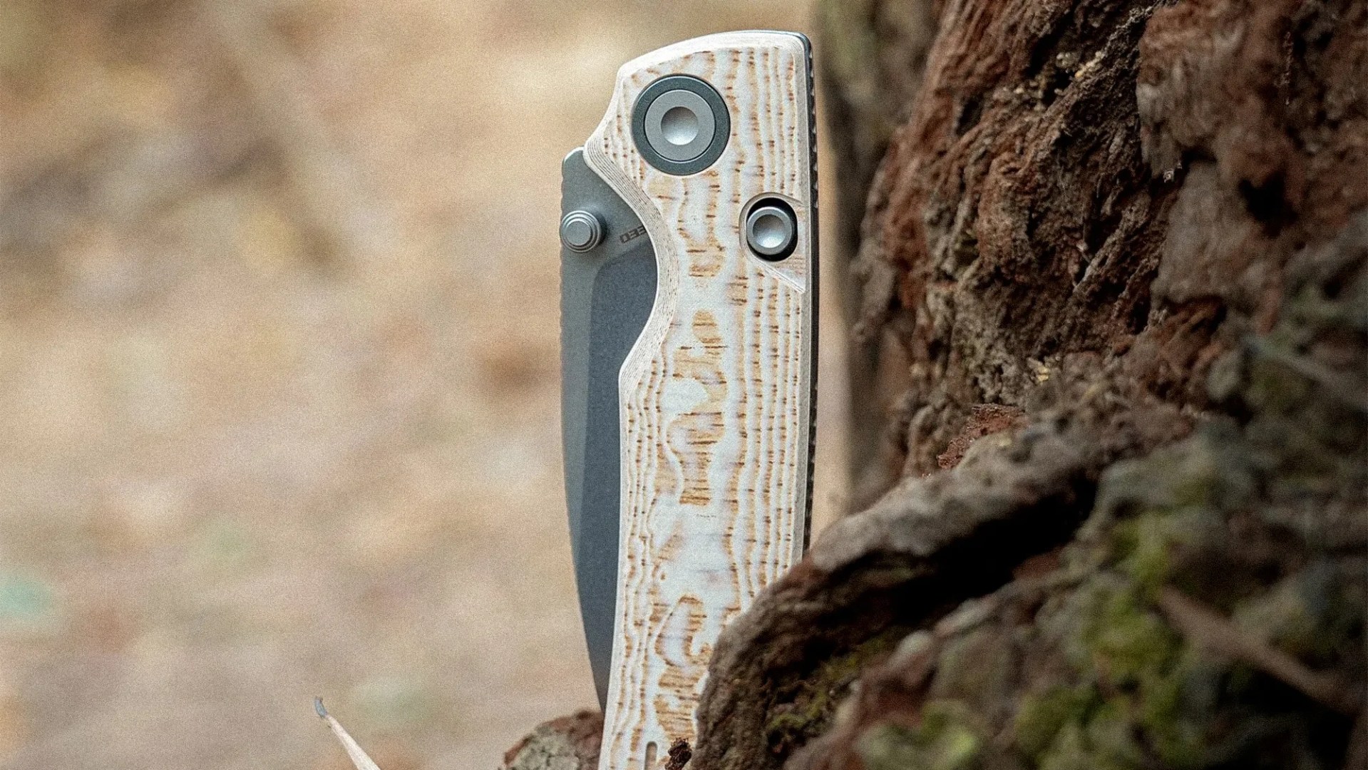 Folding knife with a textured light wood handle partially embedded in tree bark.