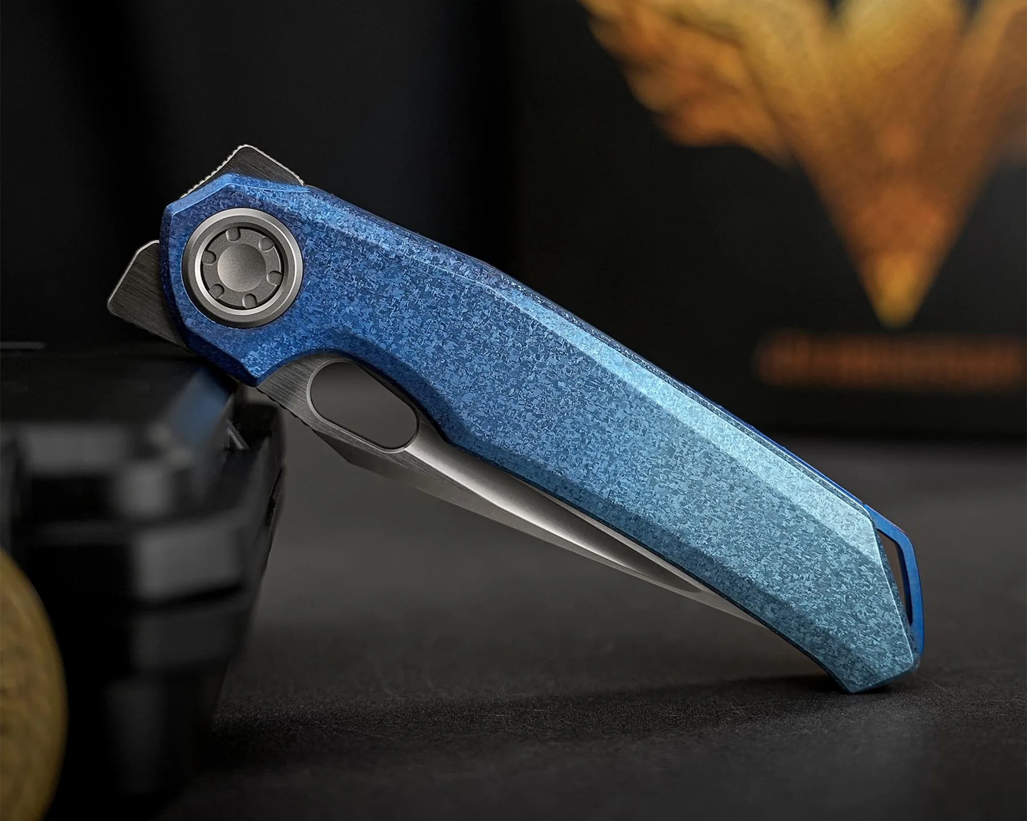 Blue textured folding knife handle with a partially visible blade on a dark surface.