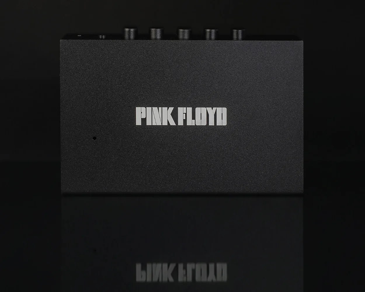 Black rectangular device with textured surface and "PINK FLOYD" printed in white on the front.