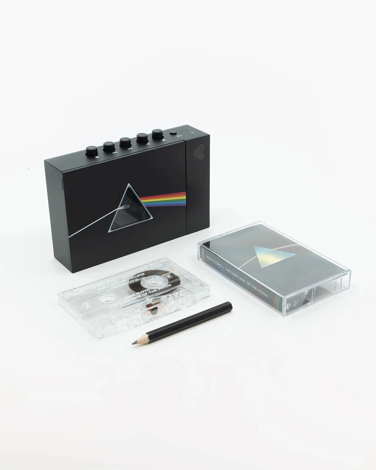Black cassette player with Pink Floyd Dark Side of the Moon prism design, cassette tape, and black pencil on white surface.