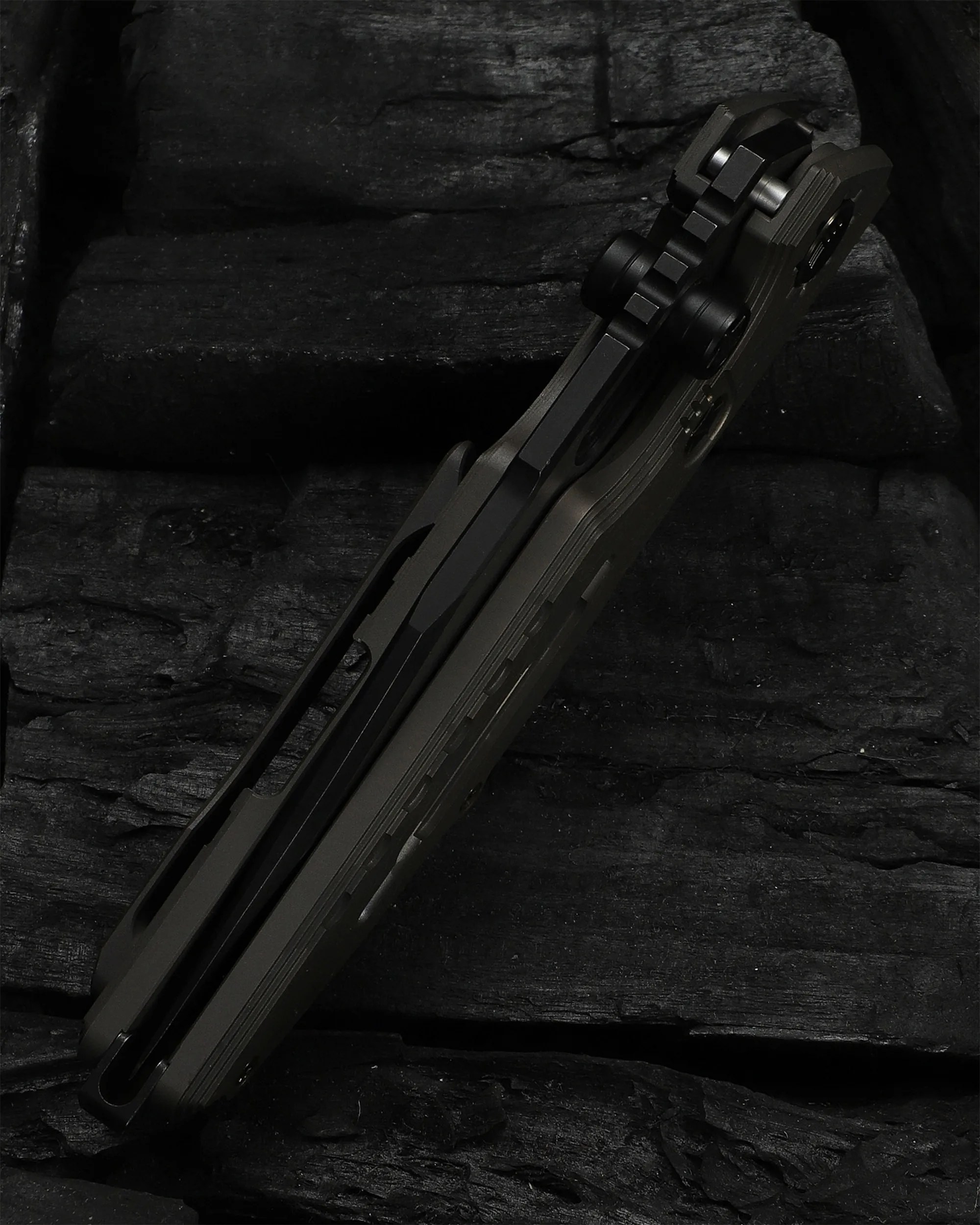 Close-up of a dark green folding knife handle with black hardware on a black textured surface.