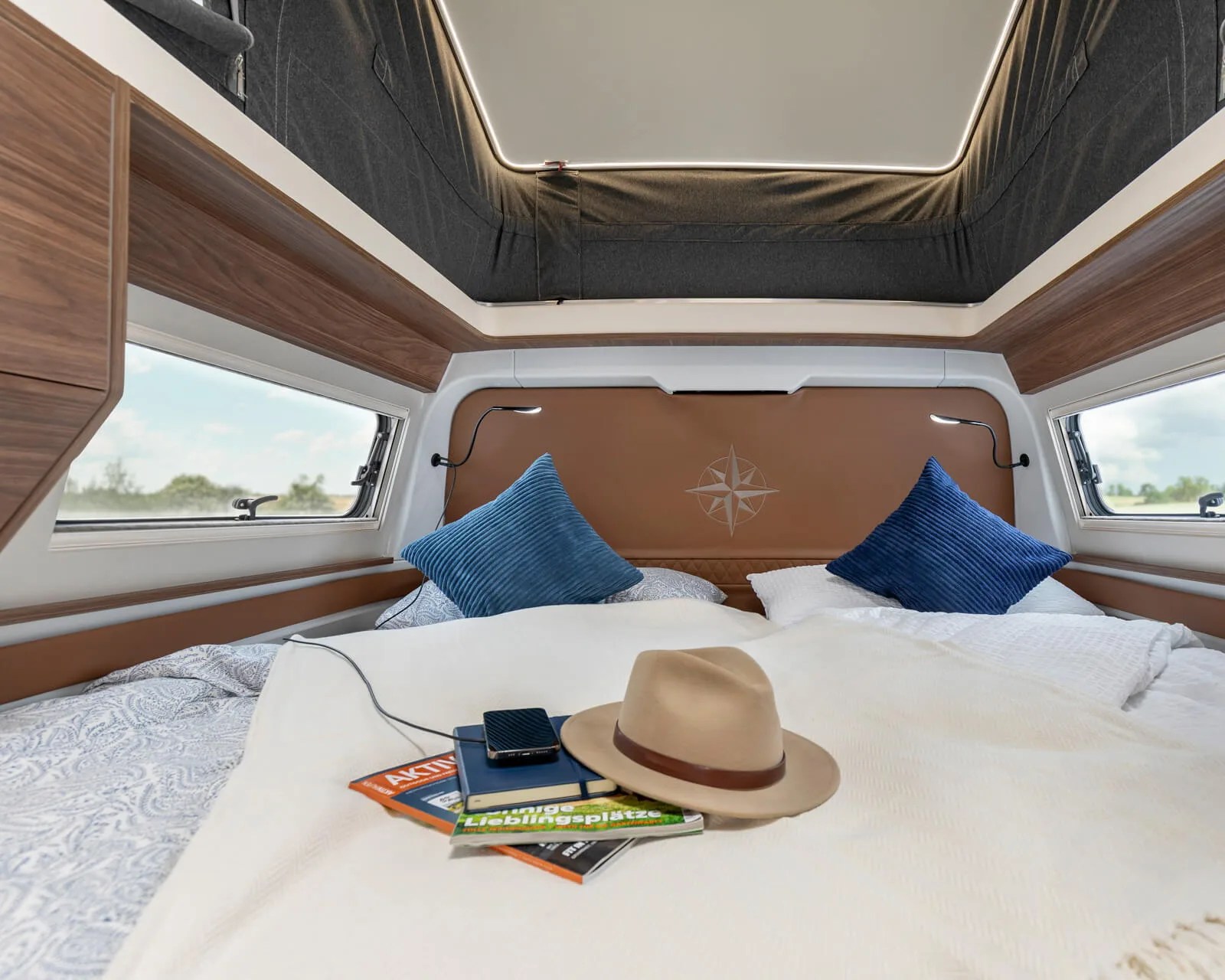 Bed with blue pillows, tan leather headboard with compass design, and a beige hat on a white blanket.