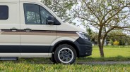 Beige camper van with brown stripes and black trim parked on grass near a tree.