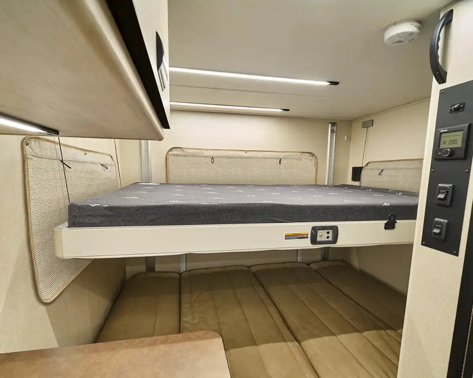 Compact bunk bed setup with a gray mattress on the upper bunk and a brown cushioned lower bunk in a beige interior.