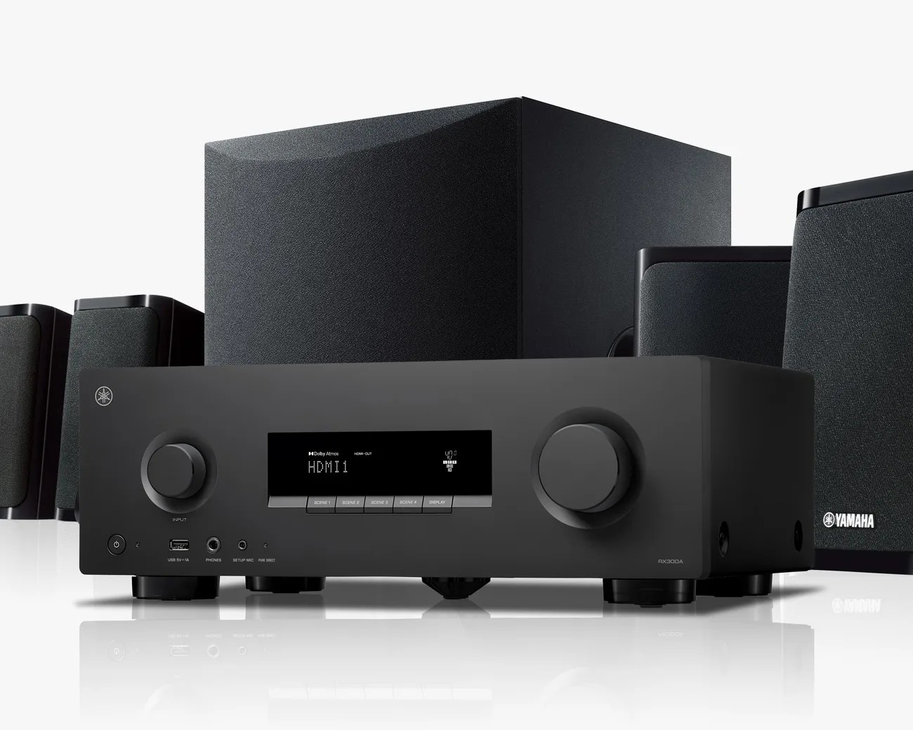 Black Yamaha RX-V6A AV receiver with multiple black speakers and subwoofer in the background on a white reflective surface.