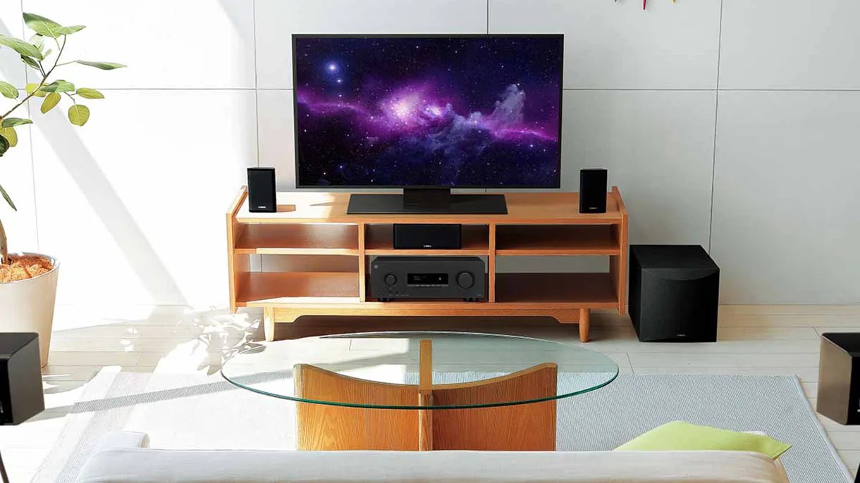 Flat-screen TV on a wooden media console with black speakers and a glass coffee table in front.