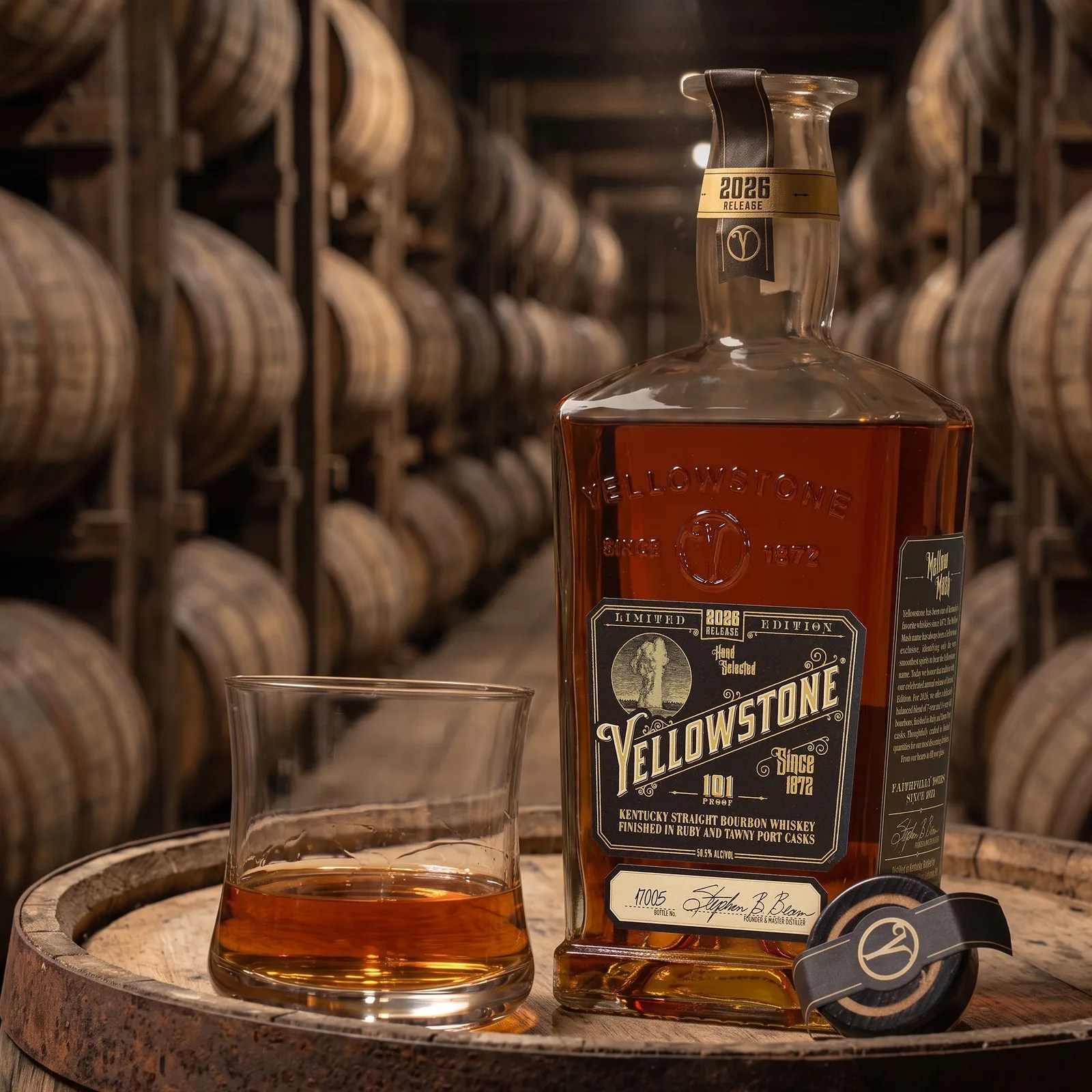 Bottle of Yellowstone Kentucky Straight Bourbon Whiskey with a glass of whiskey on a wooden barrel in a whiskey aging warehouse.